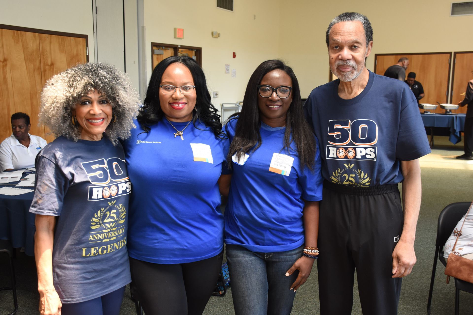 Four people in blue shirts pose indoors, possibly at an event.