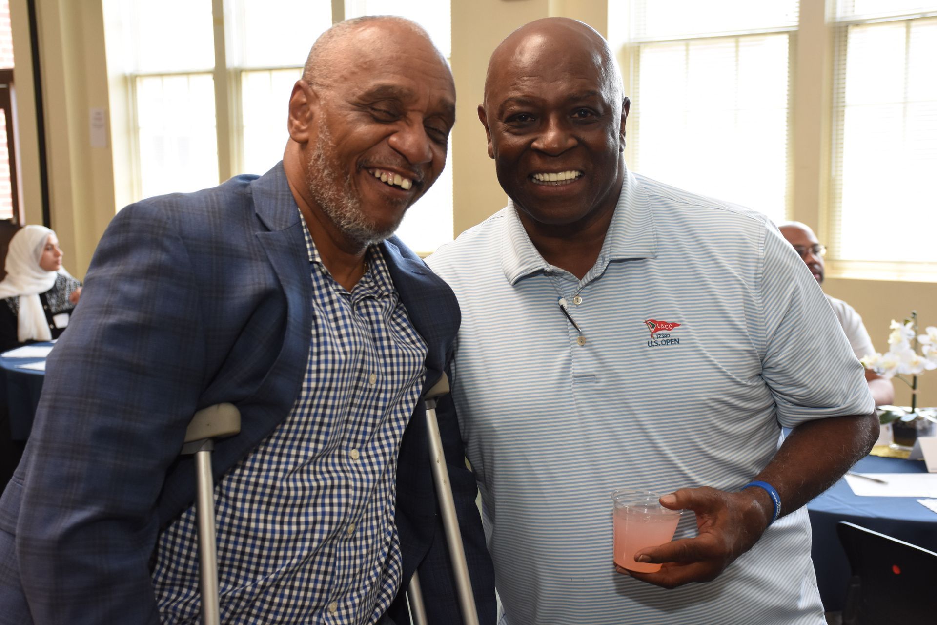Two men smiling, one with a crutch, in a brightly lit room.