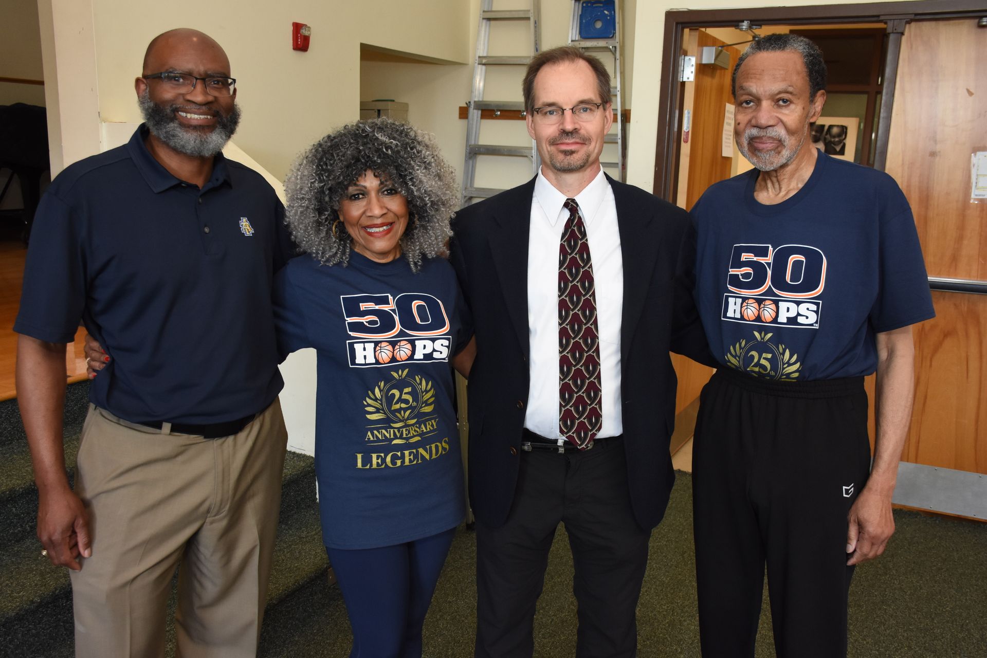 Four people posing together indoors, two wearing 