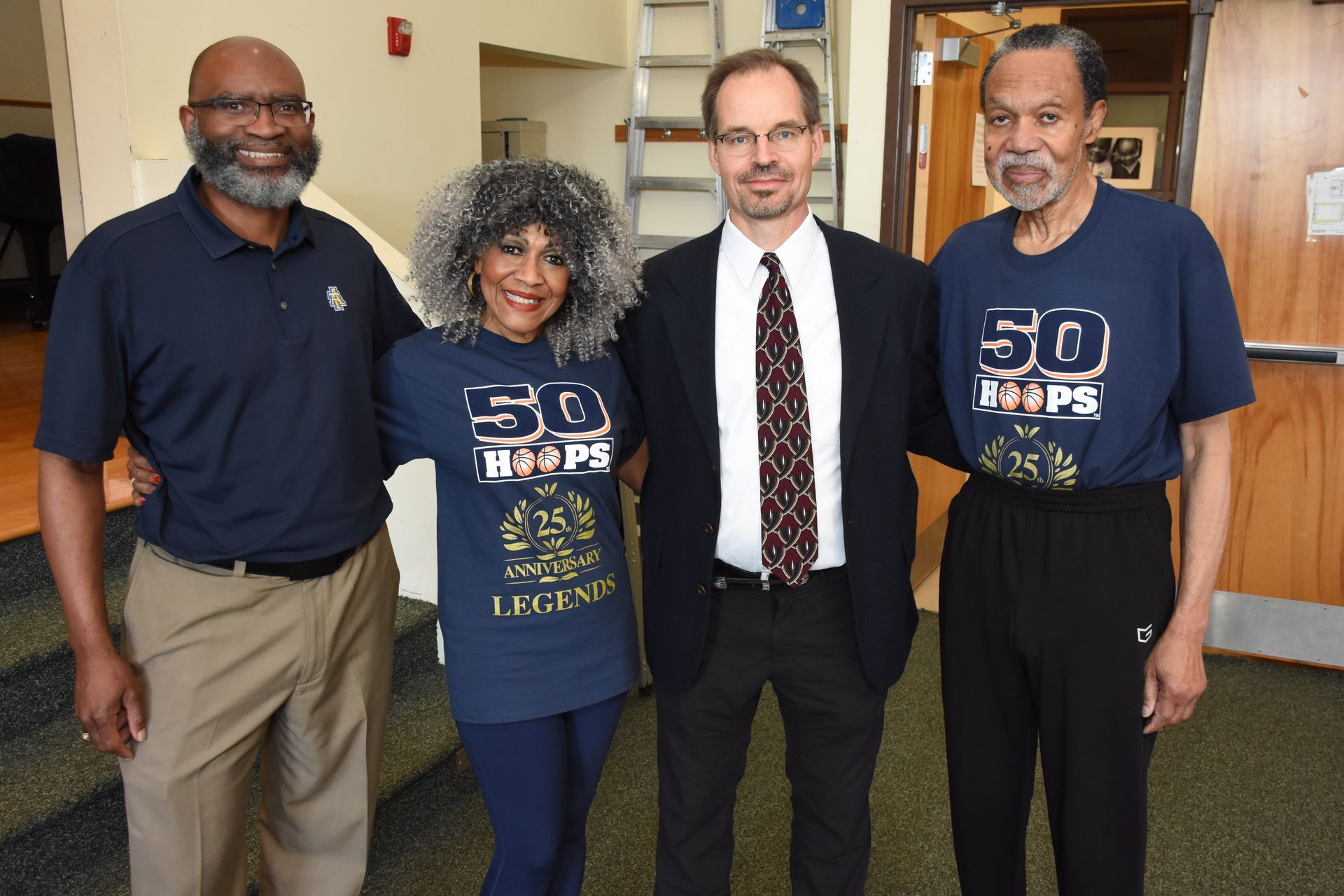 Four people pose together indoors: two wearing 