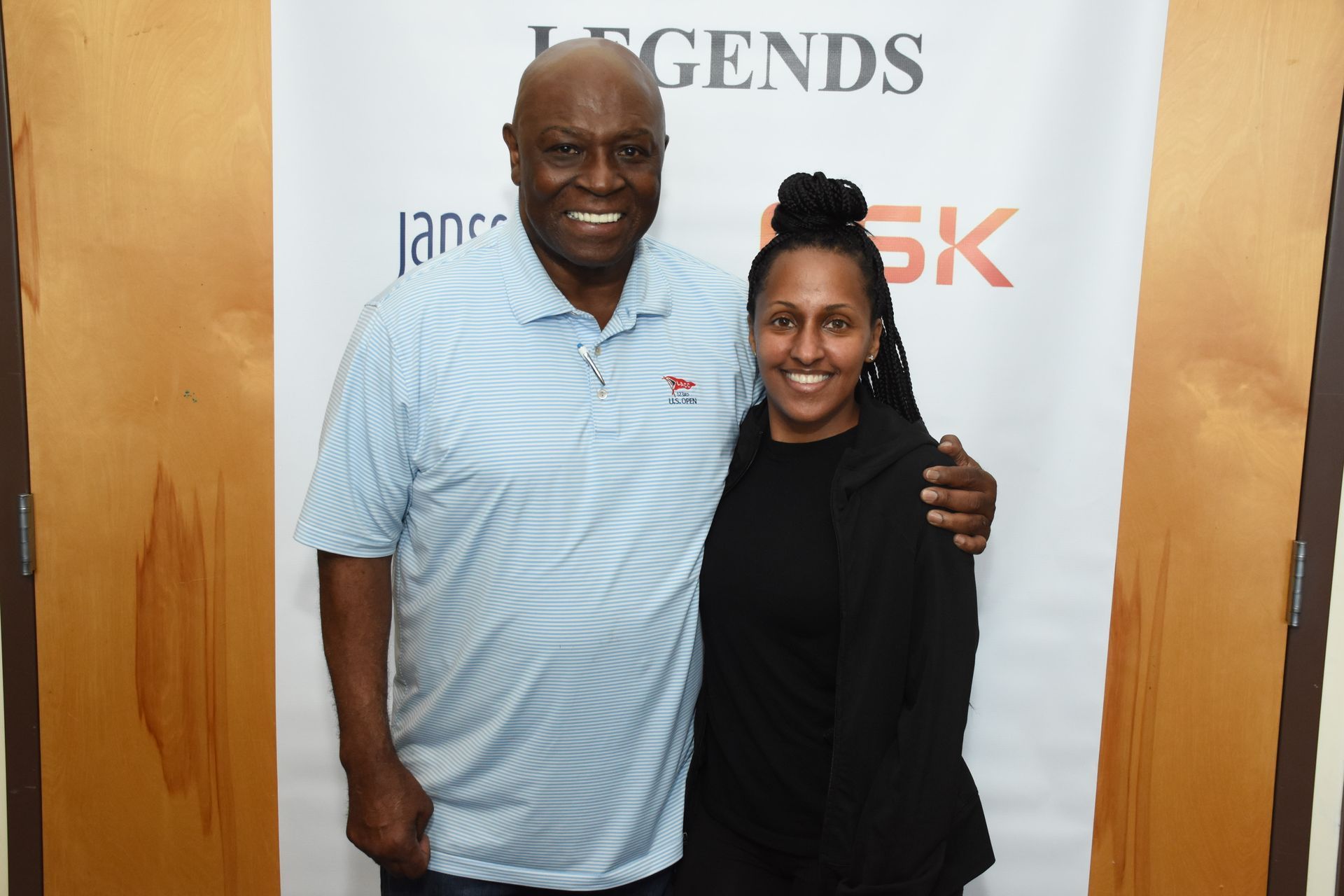Man in blue shirt and woman in black jacket pose together, smiling at a Legends 5K event.