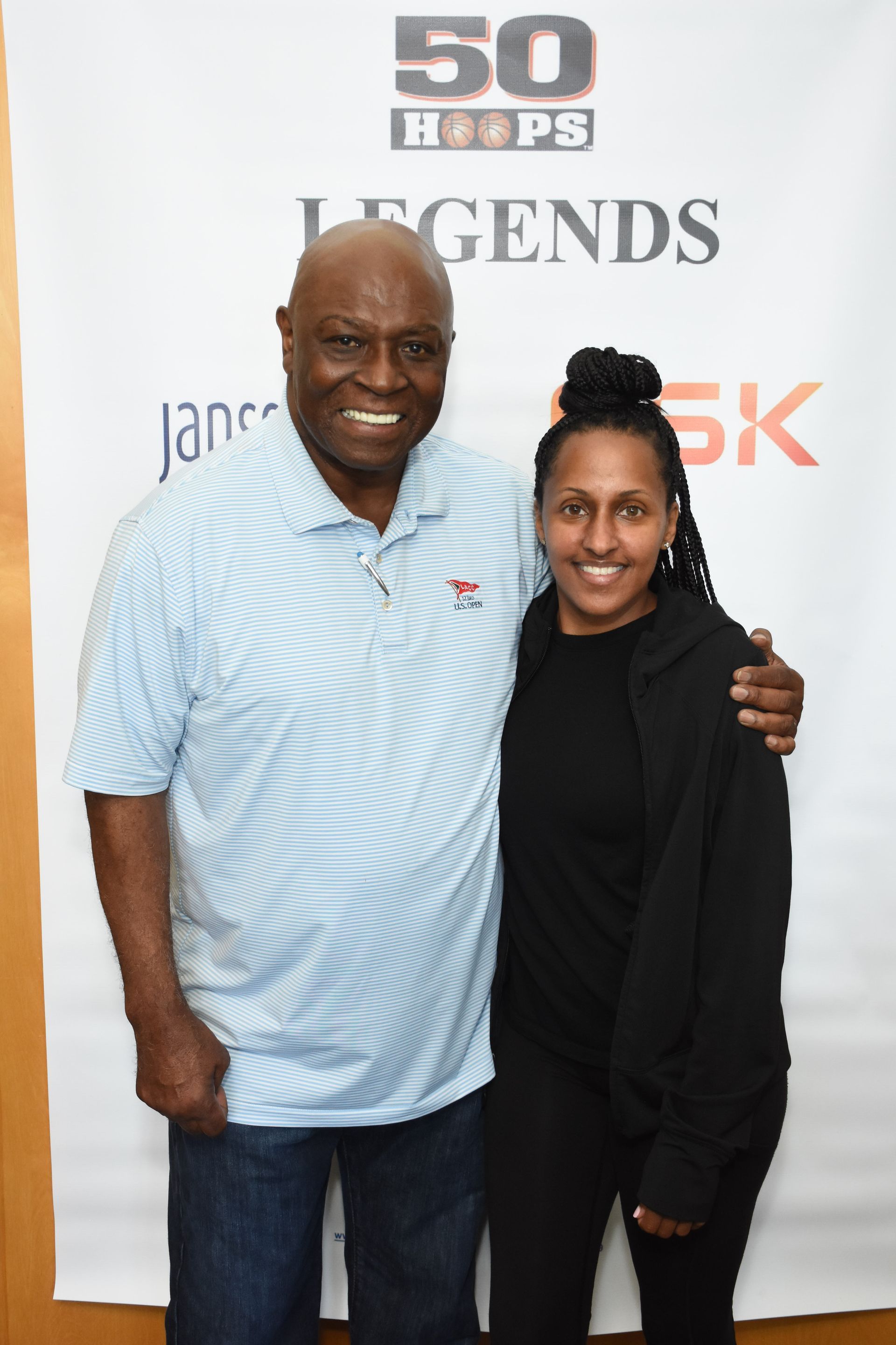 Man in blue shirt and woman in black jacket pose together in front of a banner.