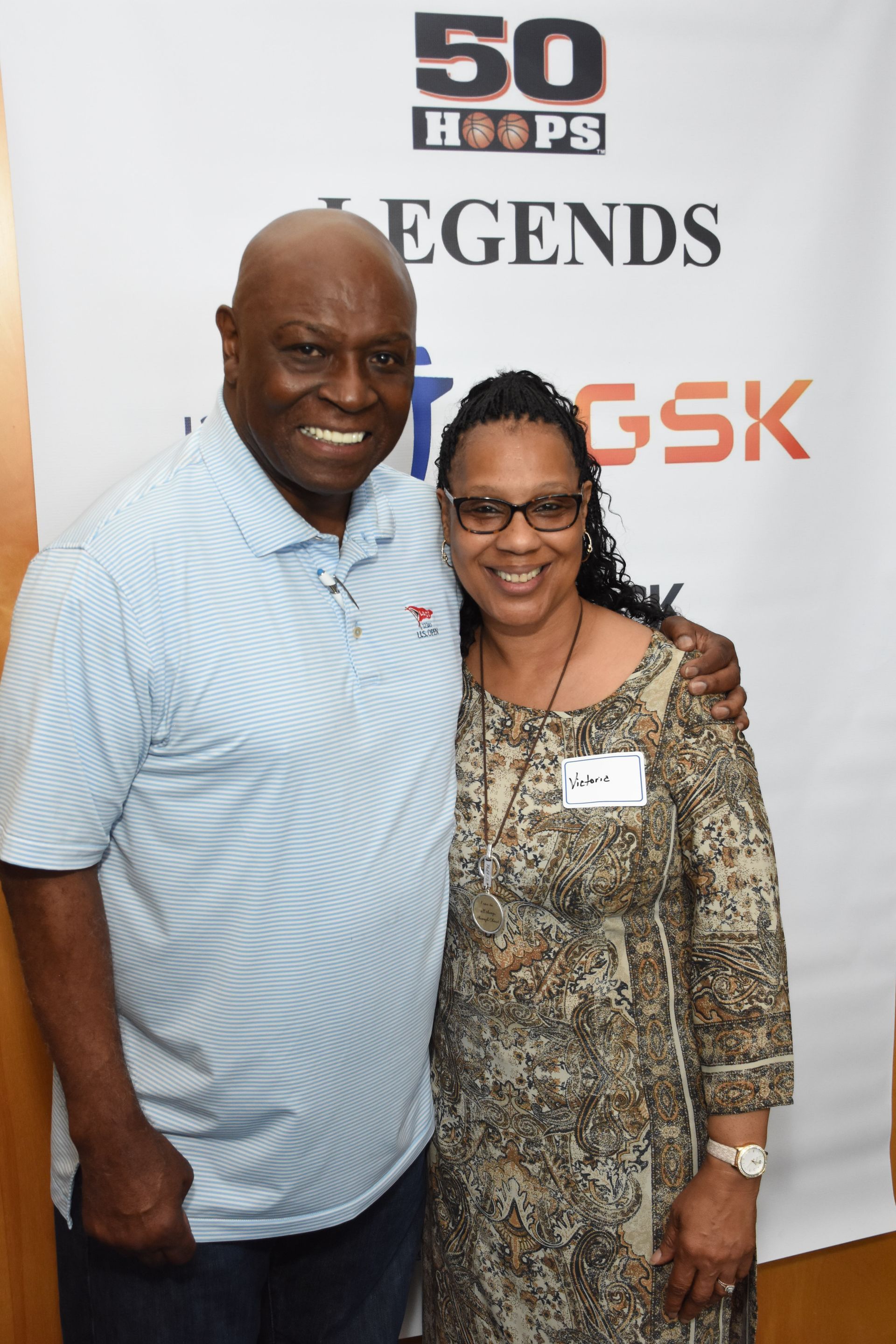 Man in light blue shirt and woman in patterned dress smile, posing together at an event with a 