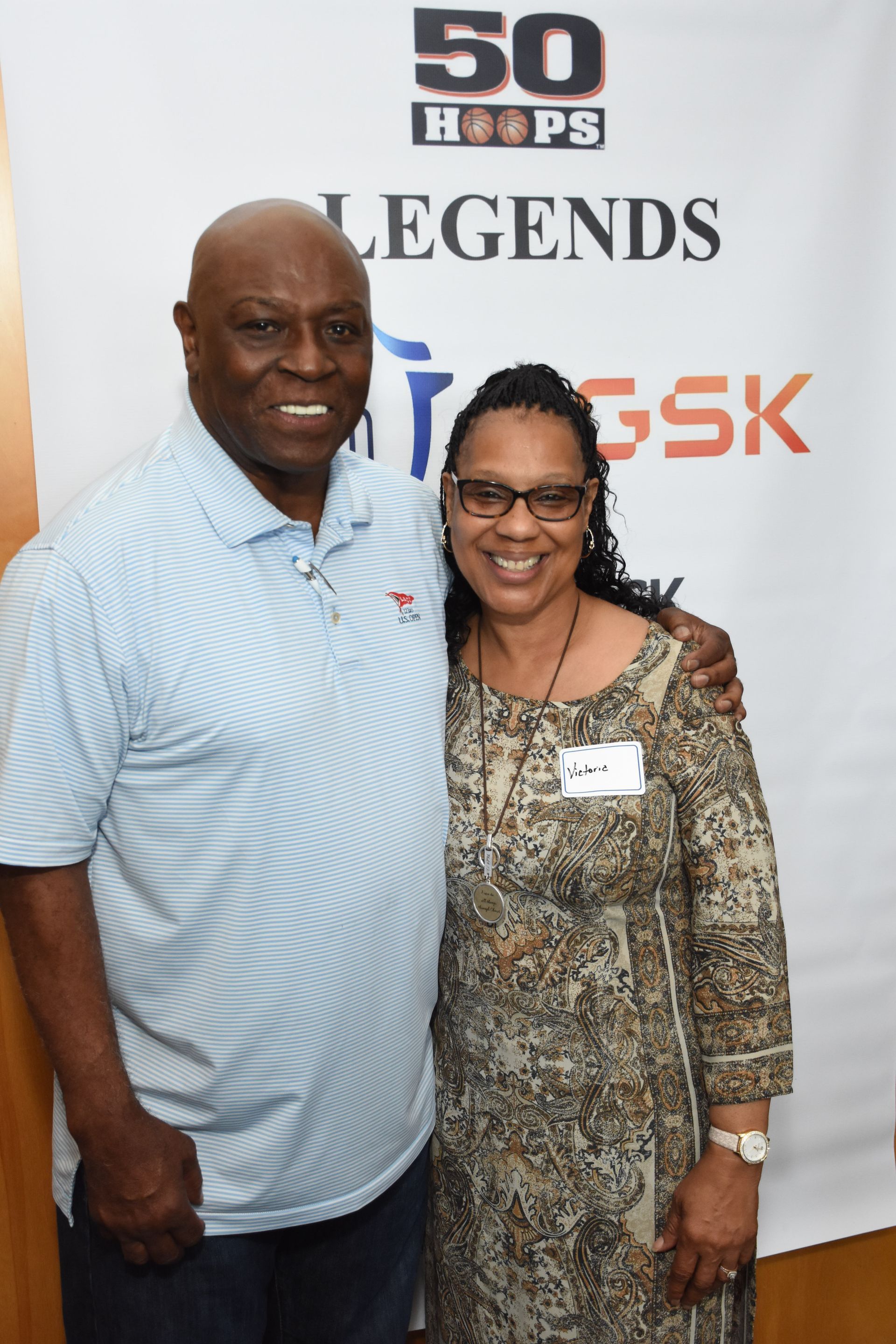 Two people smiling, posing together indoors, in front of a banner.