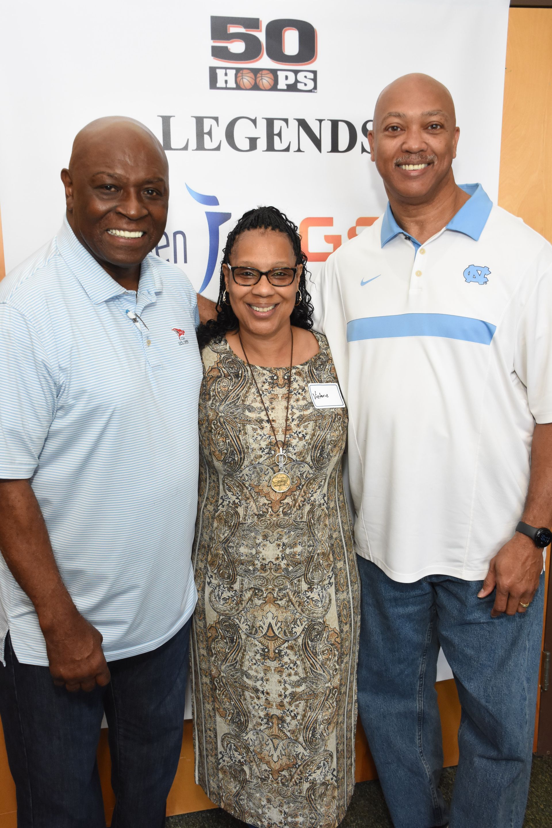 Three people smiling, posed together in front of a banner.