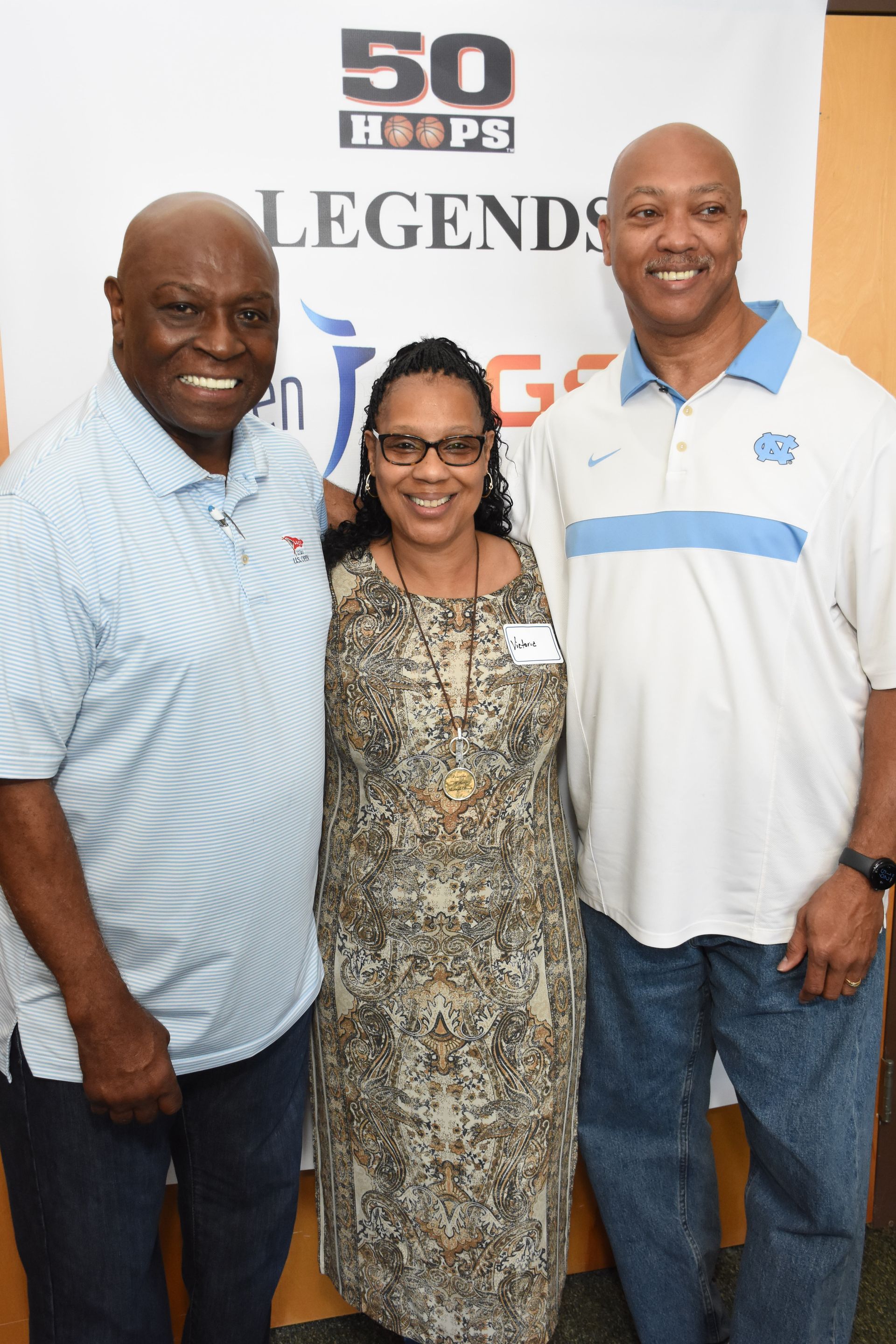 Three people pose in front of a banner. Two men flank a woman, all smiling.
