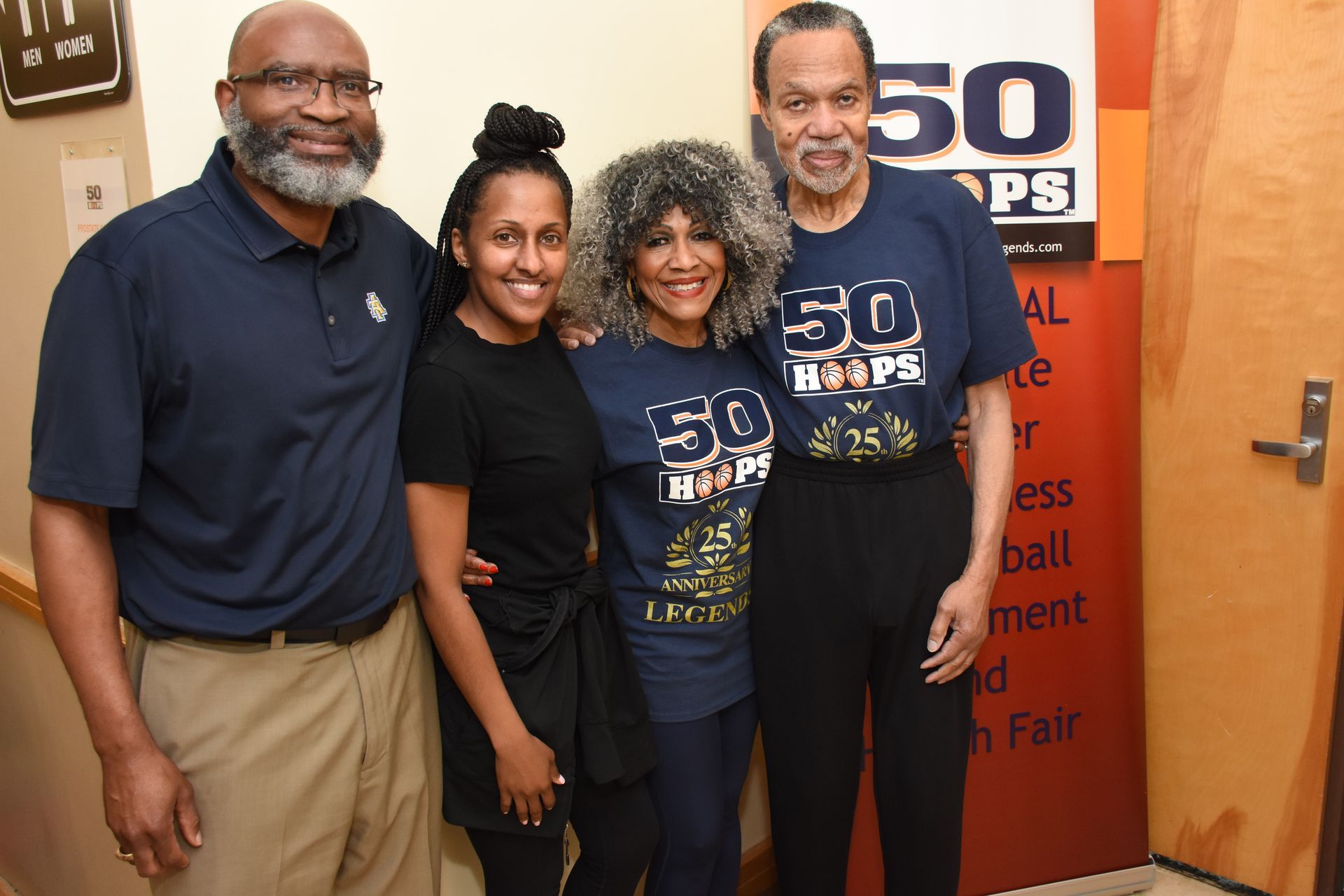 Four people pose together, smiling. Two wear 