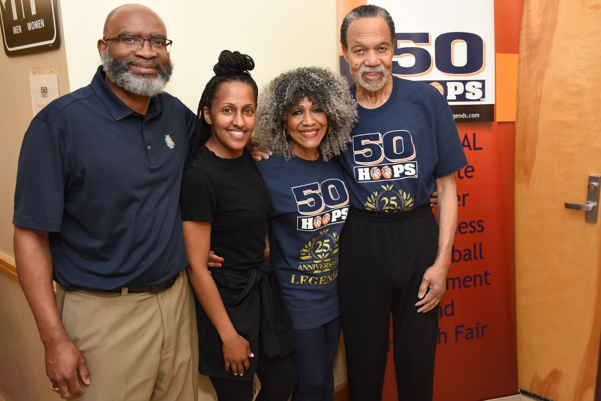 Four people smiling, posing together. Two are wearing 
