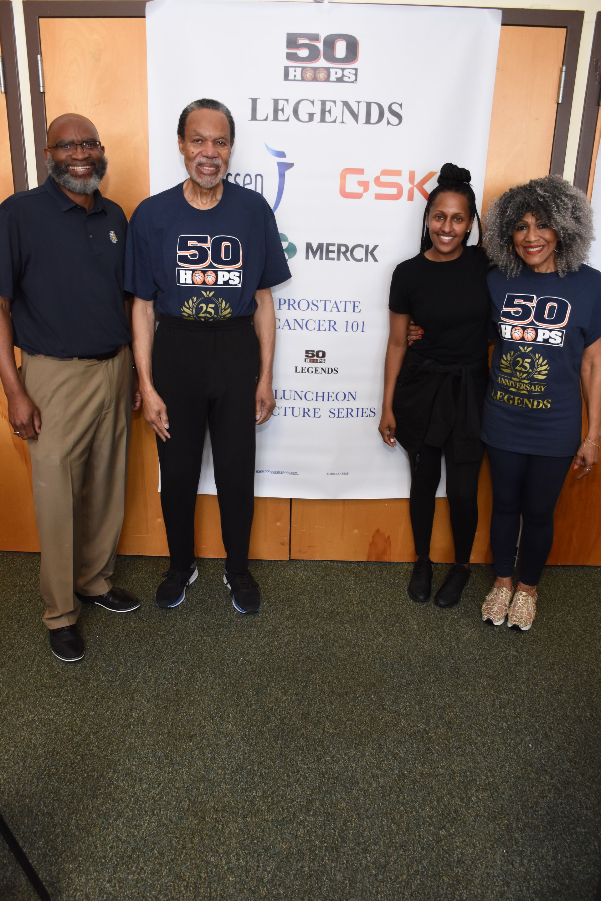 Four people standing in front of a banner; black background, two men and two women; event sponsors displayed.