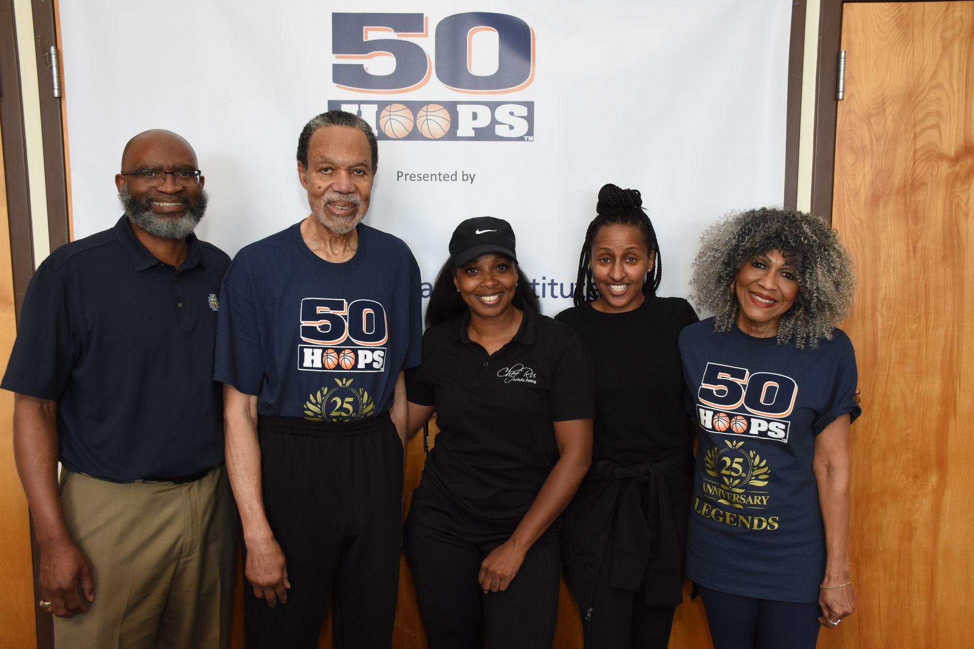 Five people pose in front of a banner that reads 