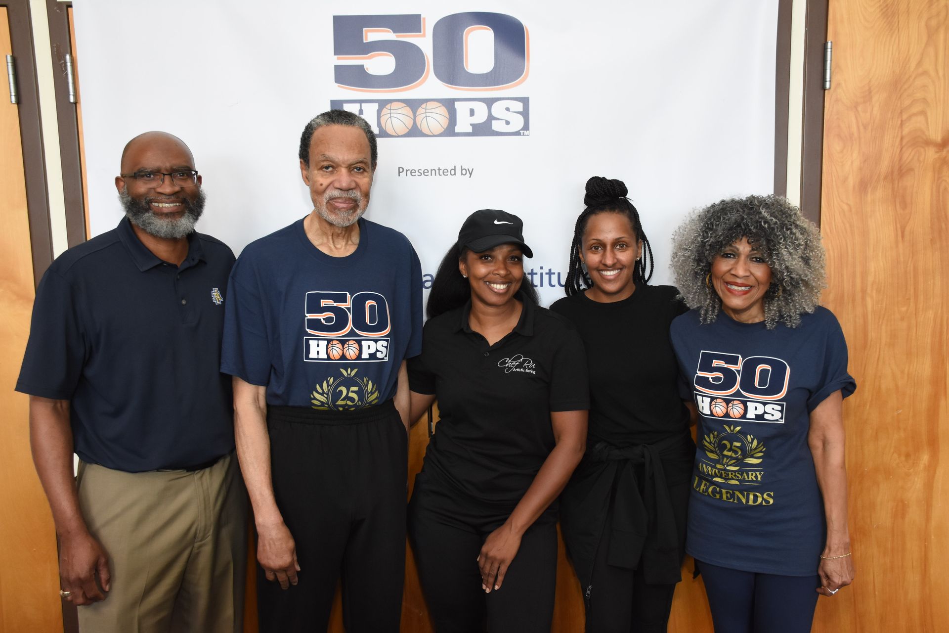 Five people pose in front of a banner. They are wearing navy shirts that read 