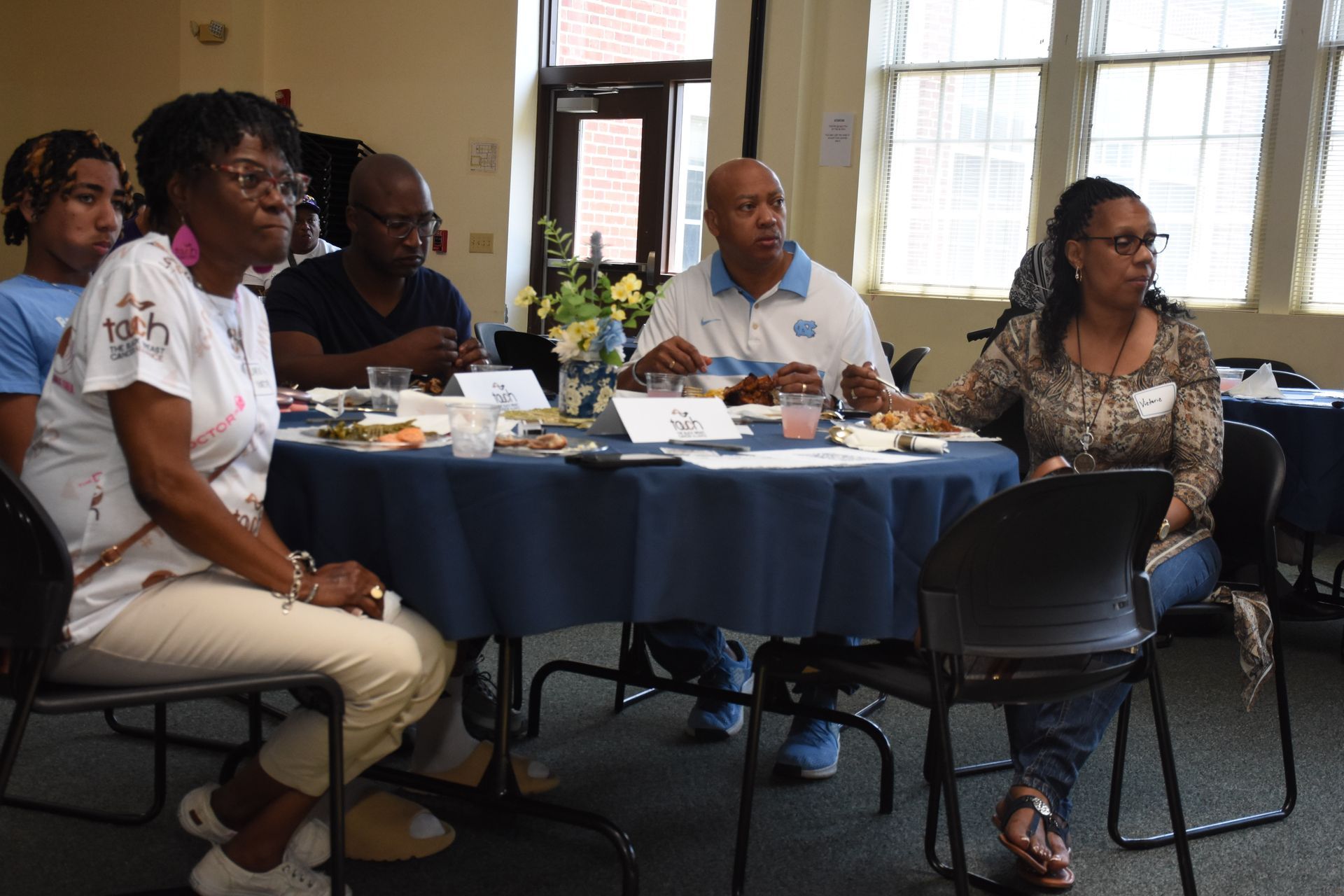 People seated around a table, attending a meeting in a room with a window, possibly a conference.