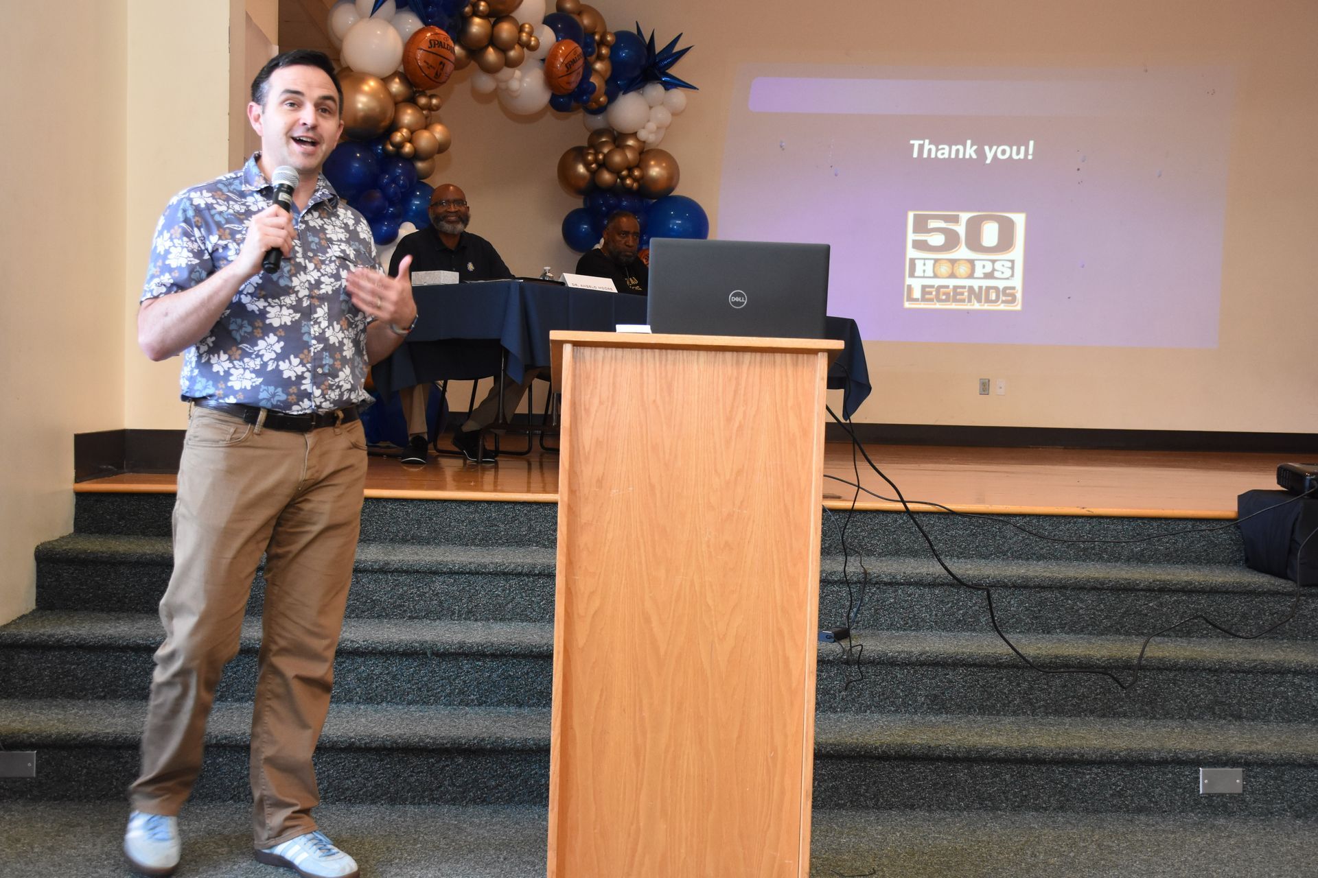 Man speaking at podium, presentation screen reads 