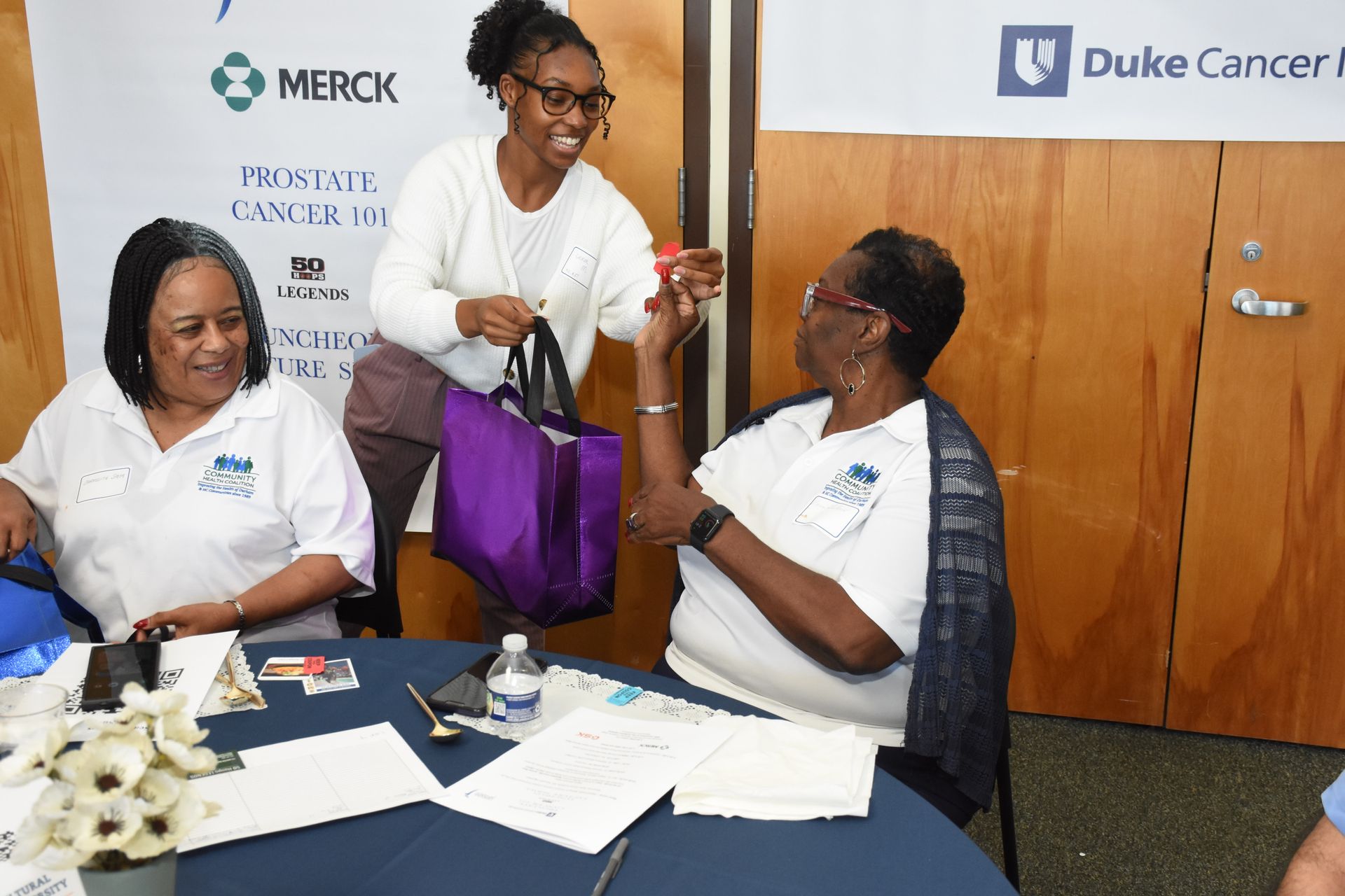 Woman hands a gift to another woman at a table with other woman.