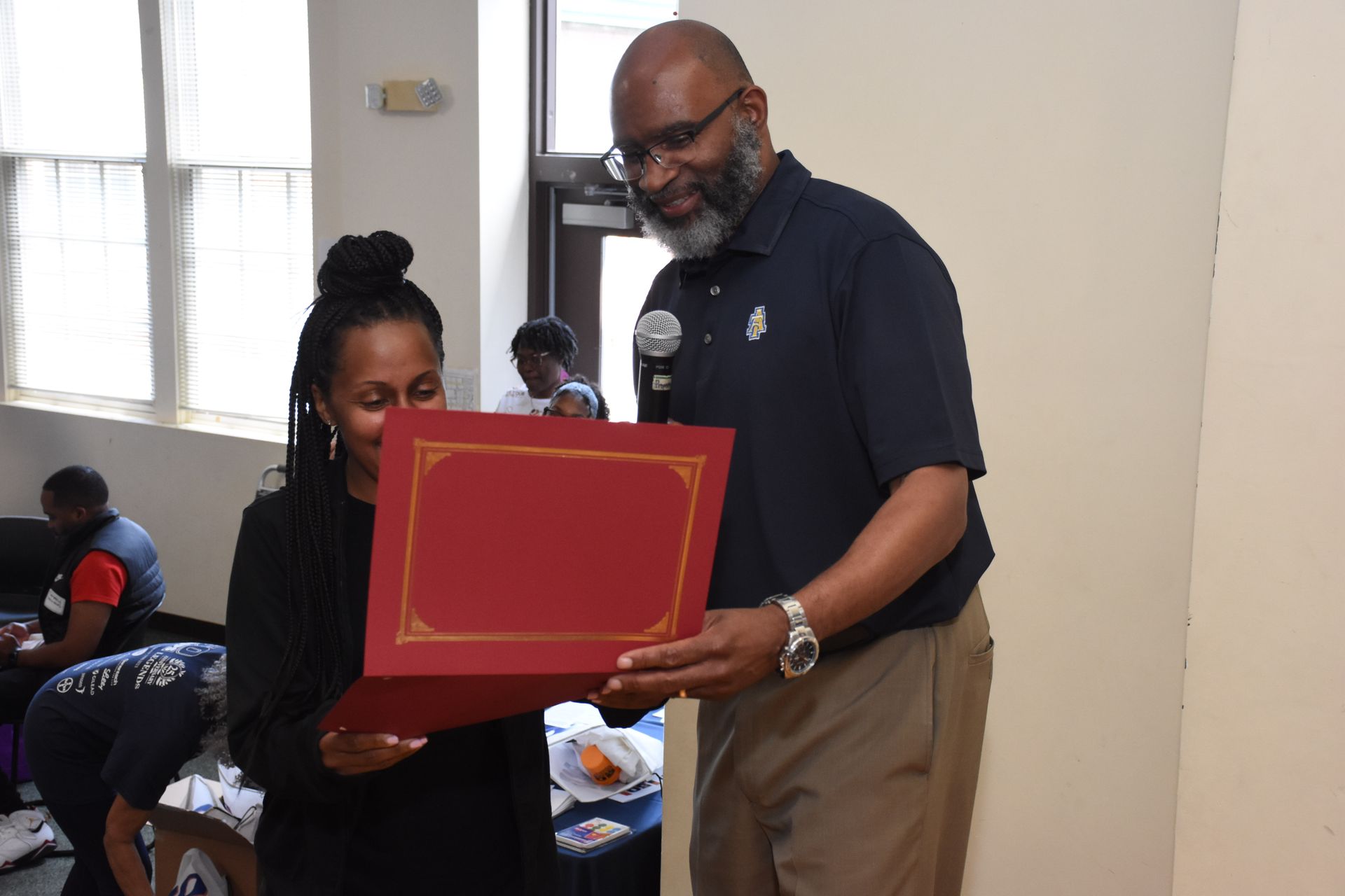 Man presenting a red certificate to a woman indoors. They are smiling.