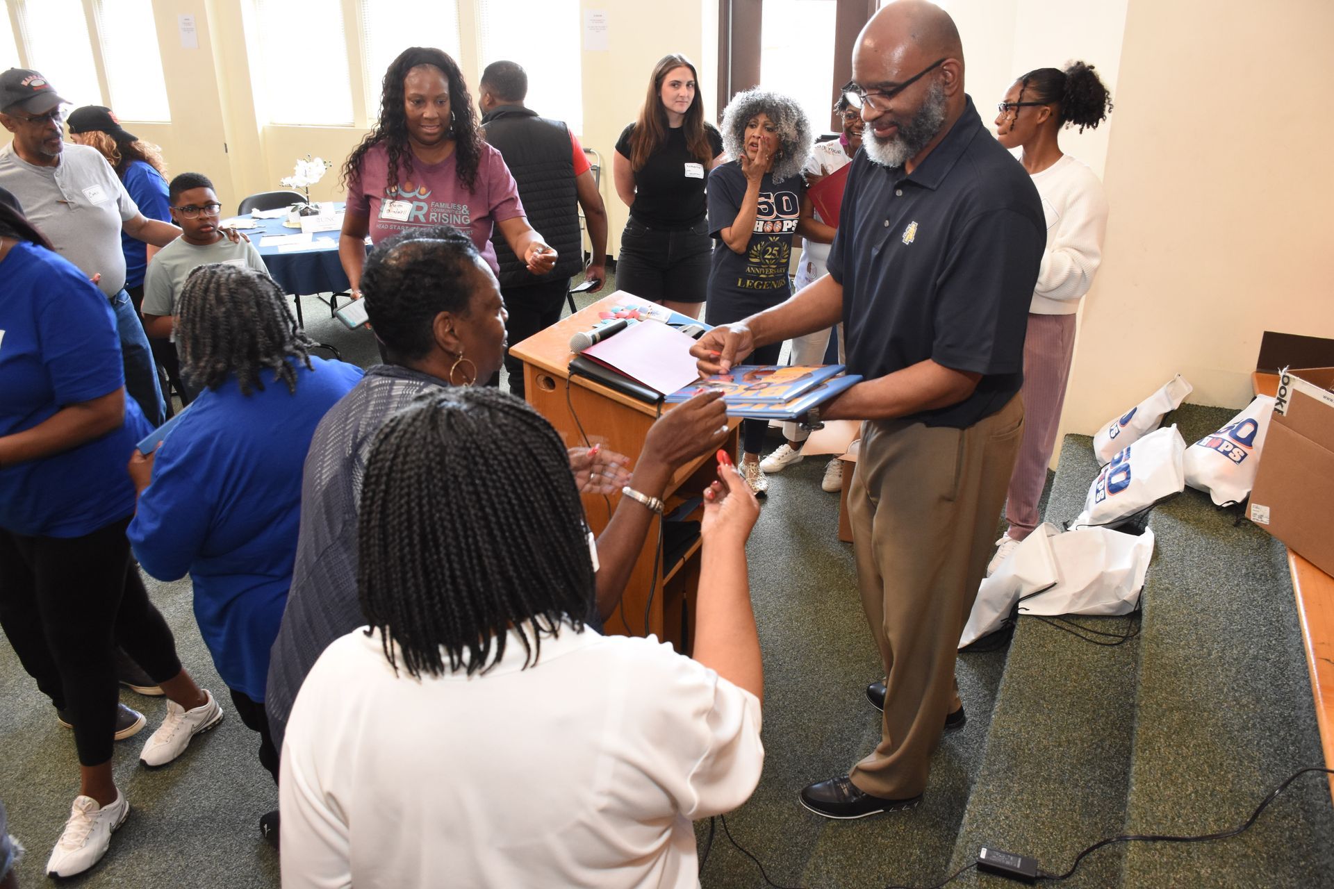 People receiving materials from a man in a navy shirt and khakis in a room.