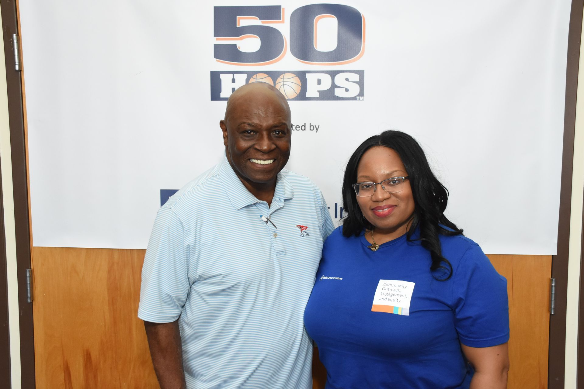 Two people smiling in front of a banner with 