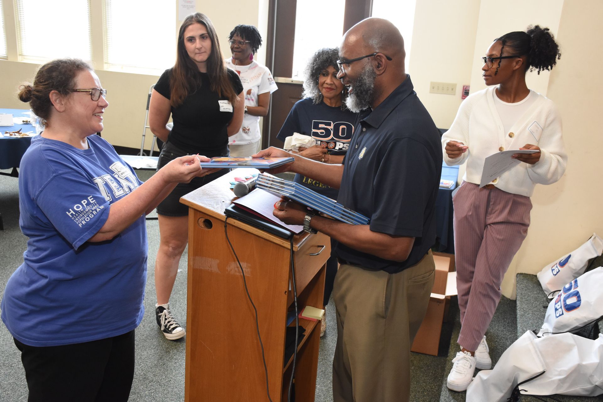 Woman in blue shirt receives a document from a man at a podium, other people watch.