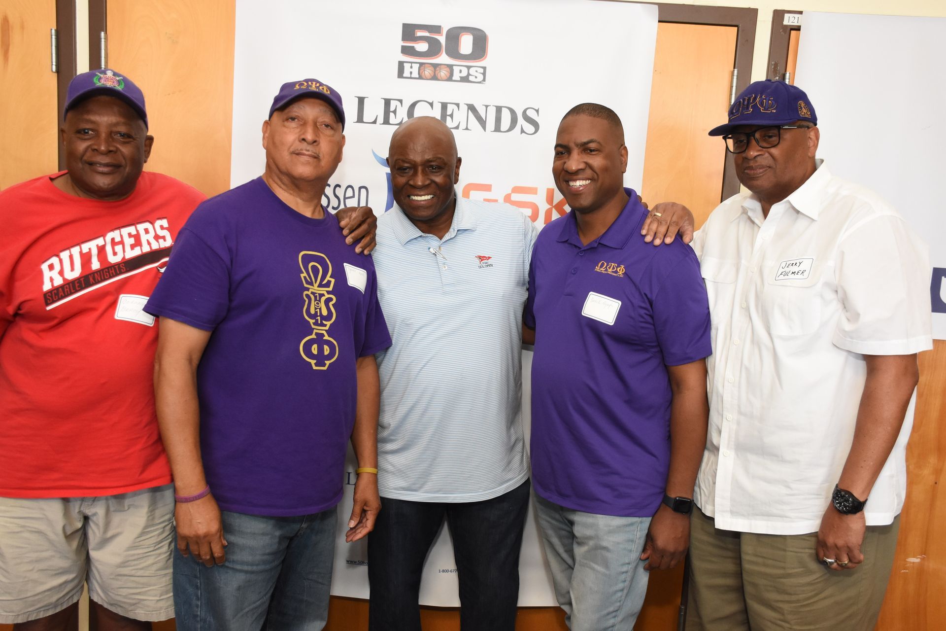 Five men in casual attire pose together; event backdrop reads 