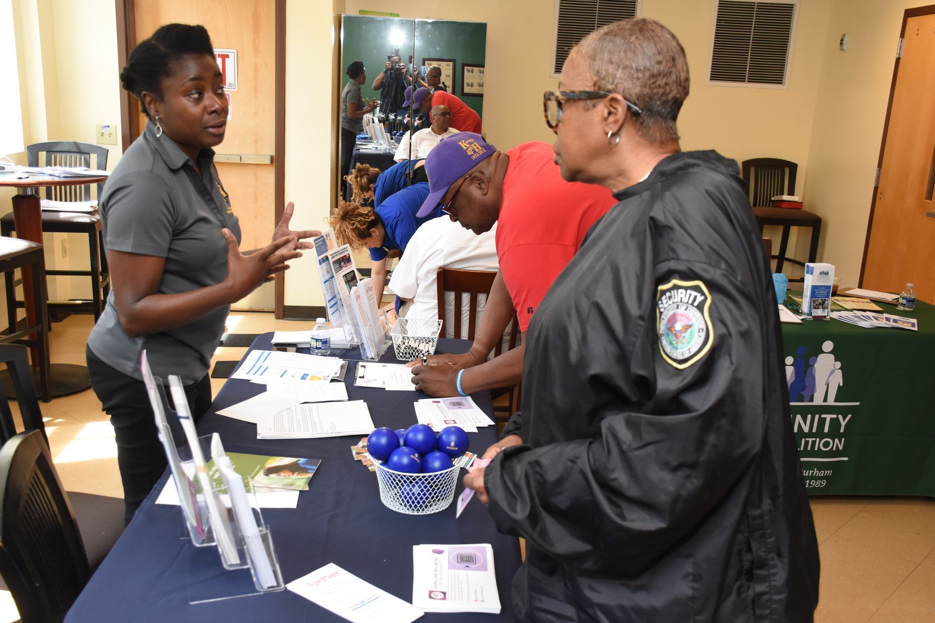 Woman at table speaks to another as people sign up at an event.