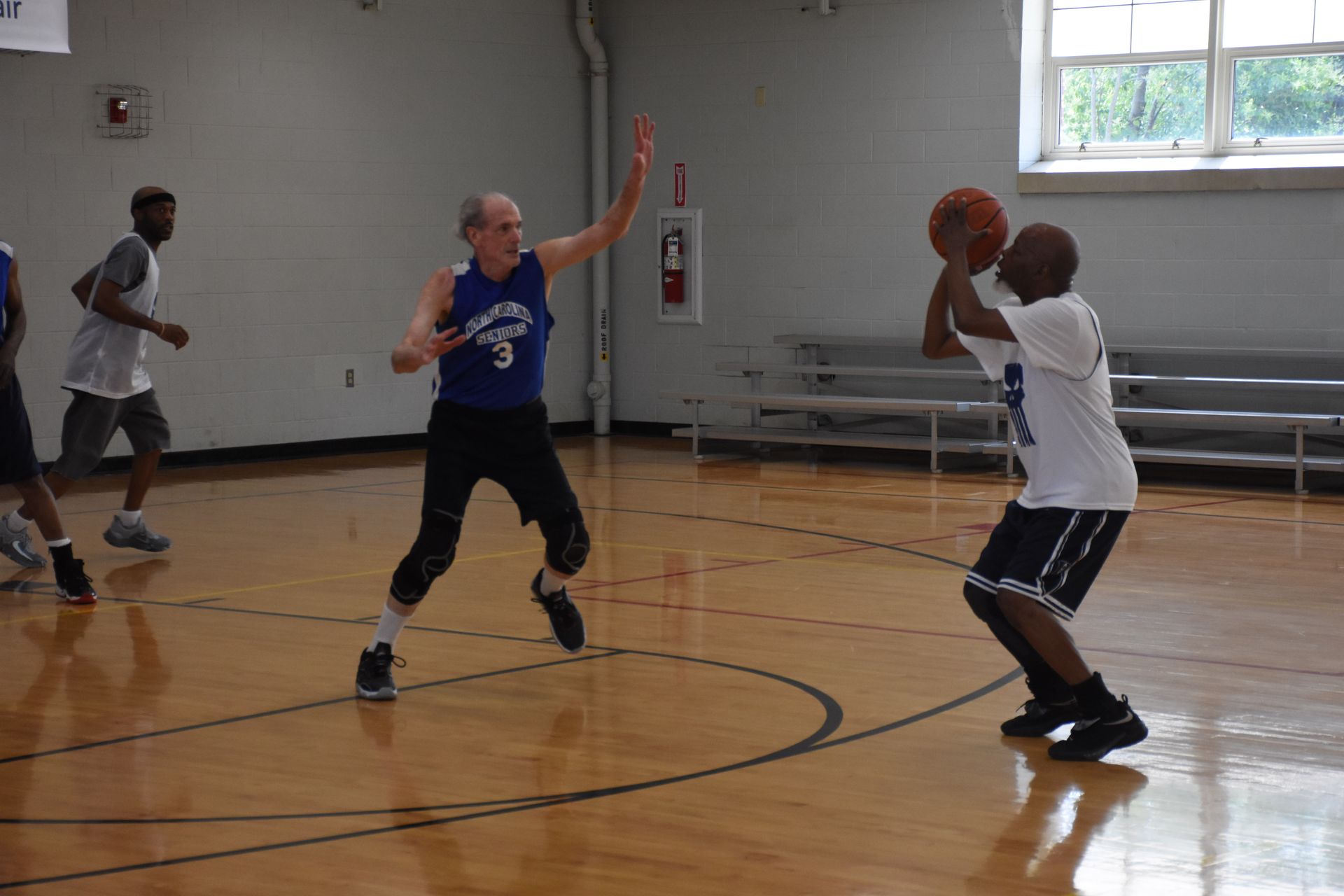 Basketball game in a gym. Player in blue defends against a player shooting the ball.