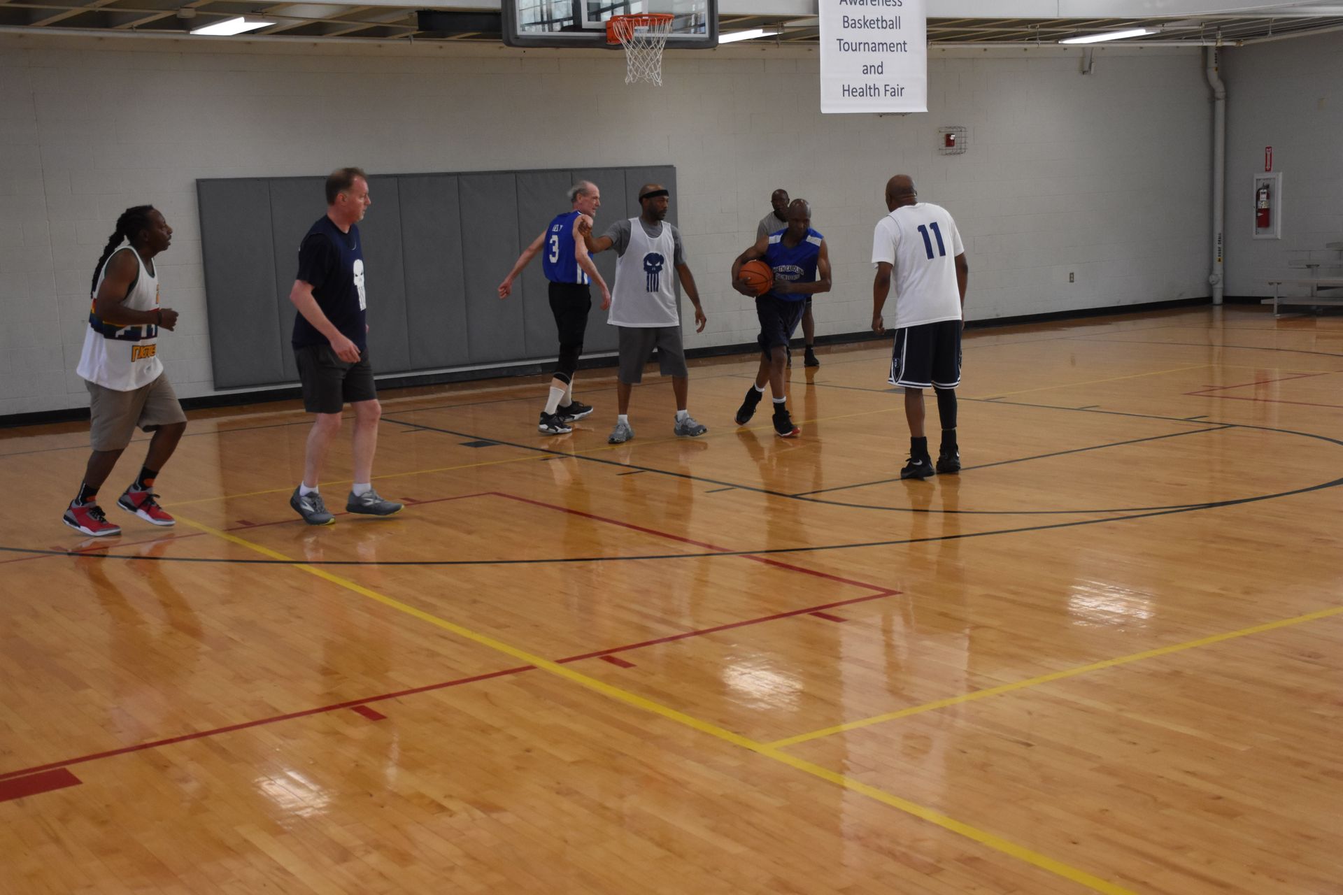 People playing basketball on a wooden court. Players dribble, pass, and prepare to shoot near the basket.