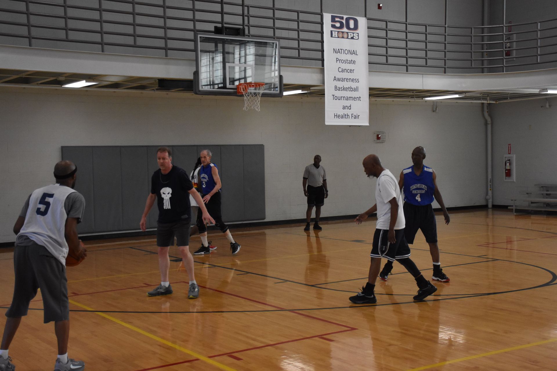 Basketball game in an indoor gym. Players in jerseys dribble and defend near the basket.