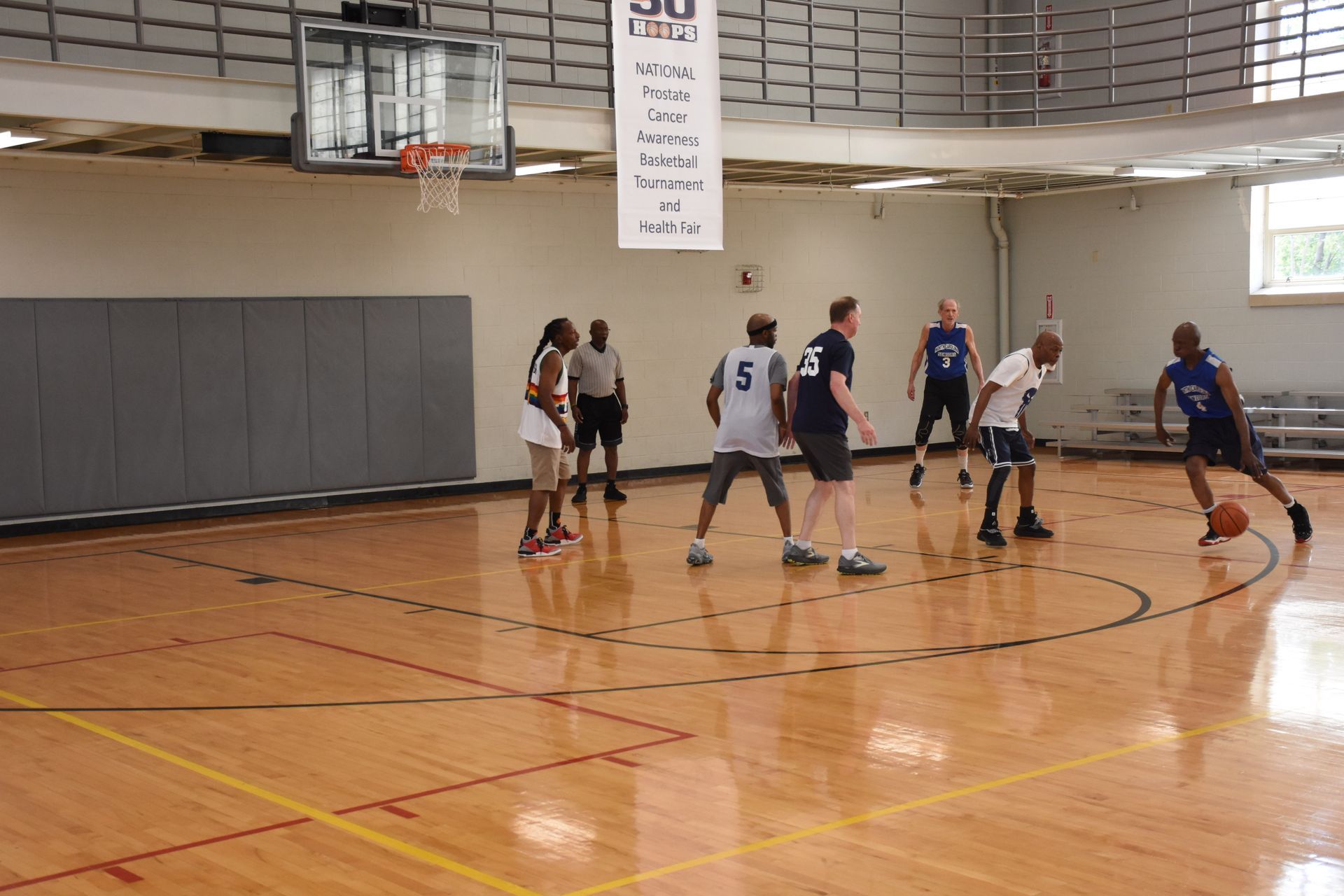Basketball game in a gym. Players dribble, defend, and shoot near the hoop, court marked with lines.