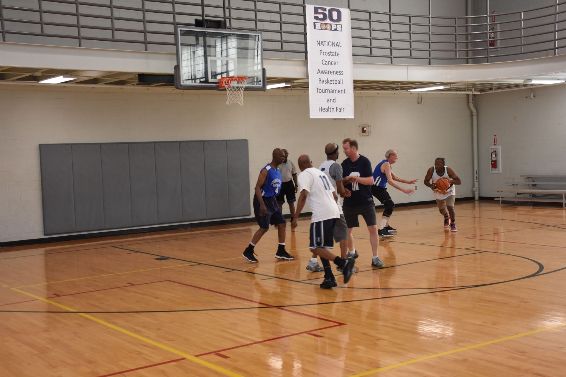 Basketball game in progress on a wooden court; players dribbling and moving toward the basket.