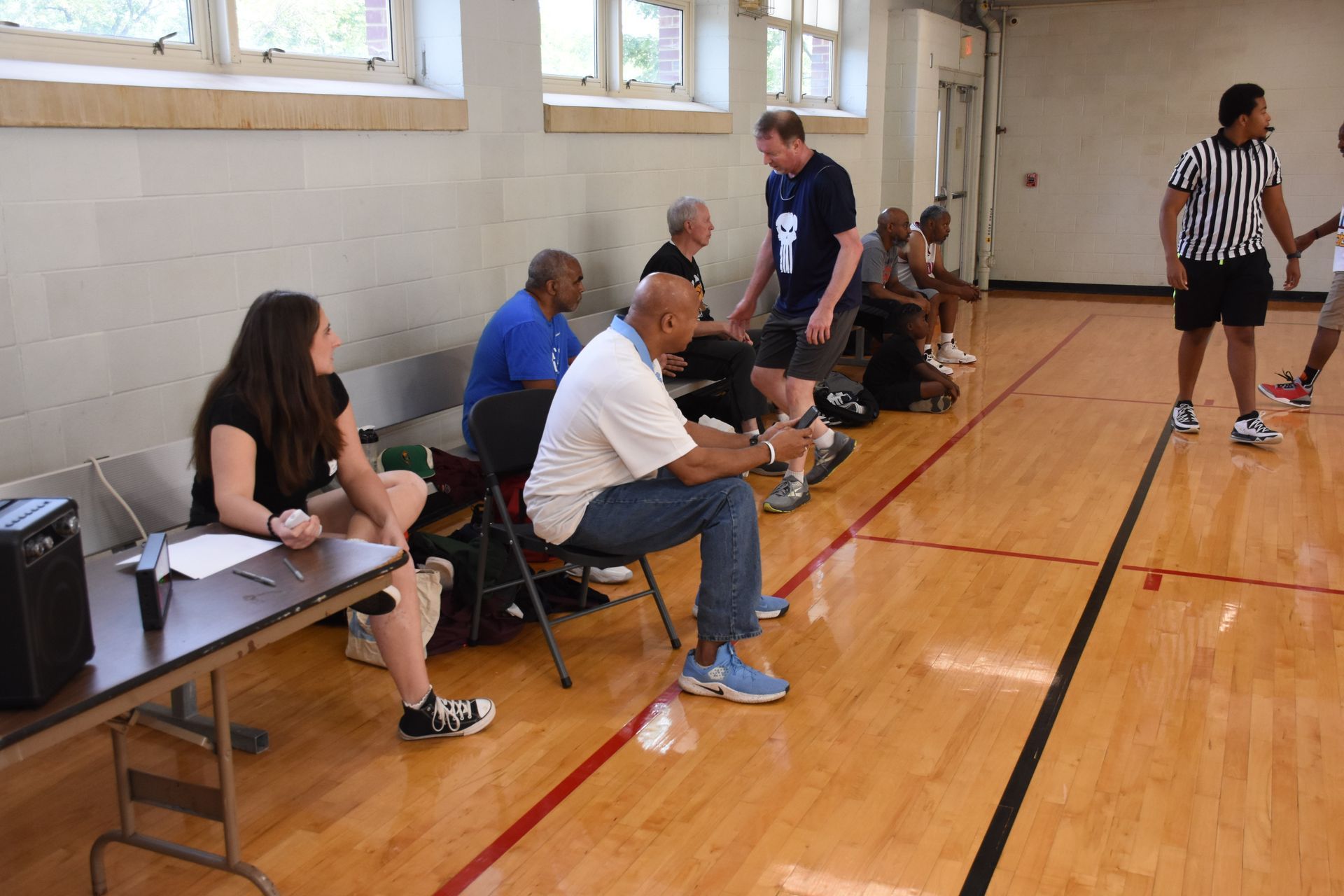 Basketball game: Players and referees on court. Spectators sit on chairs.