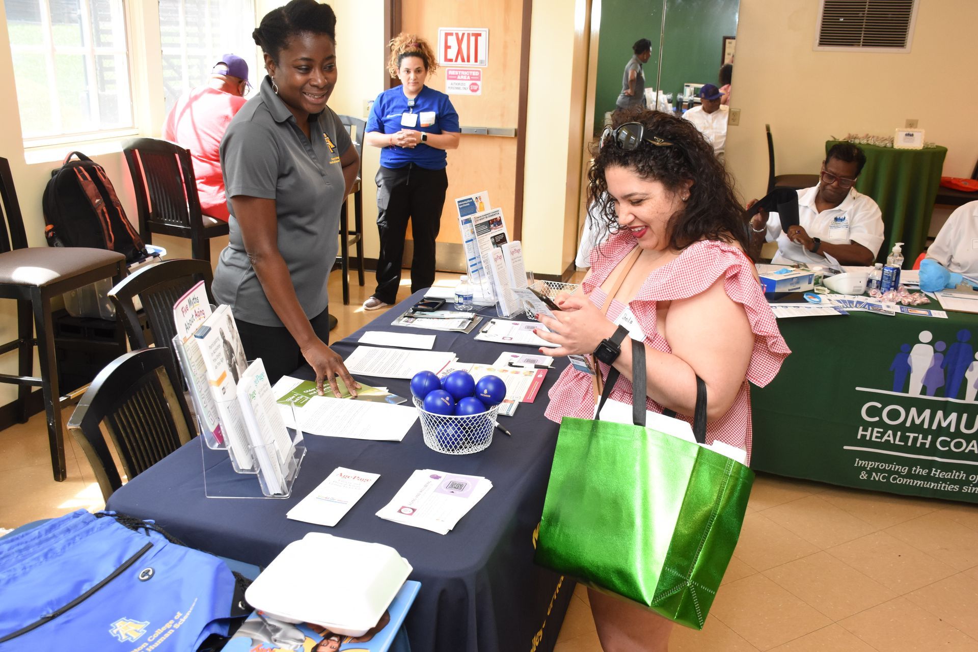 Woman looking at phone at a health fair booth; another woman assists.