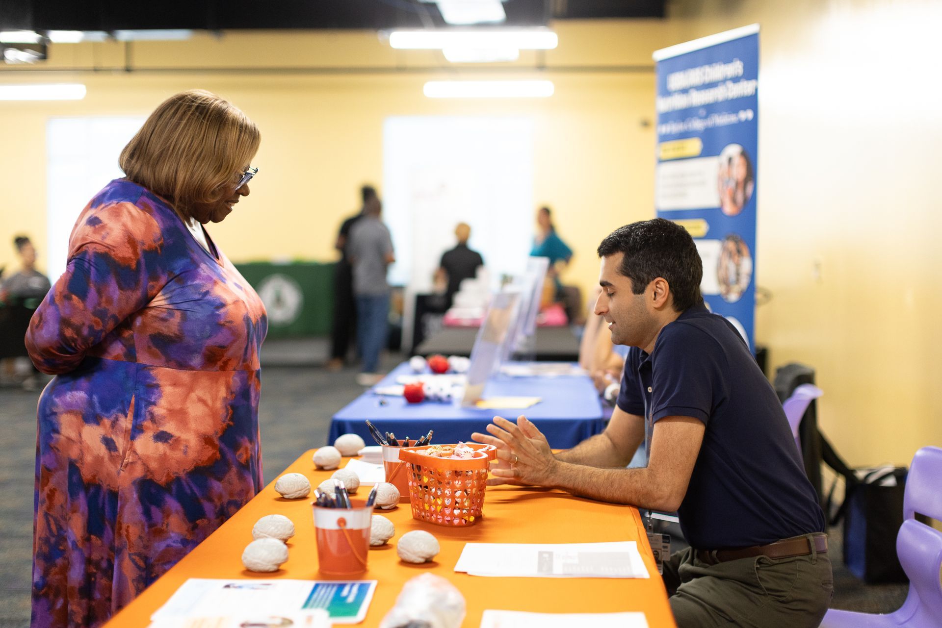 Woman talking to a man at a table with brochures and models in an event space.