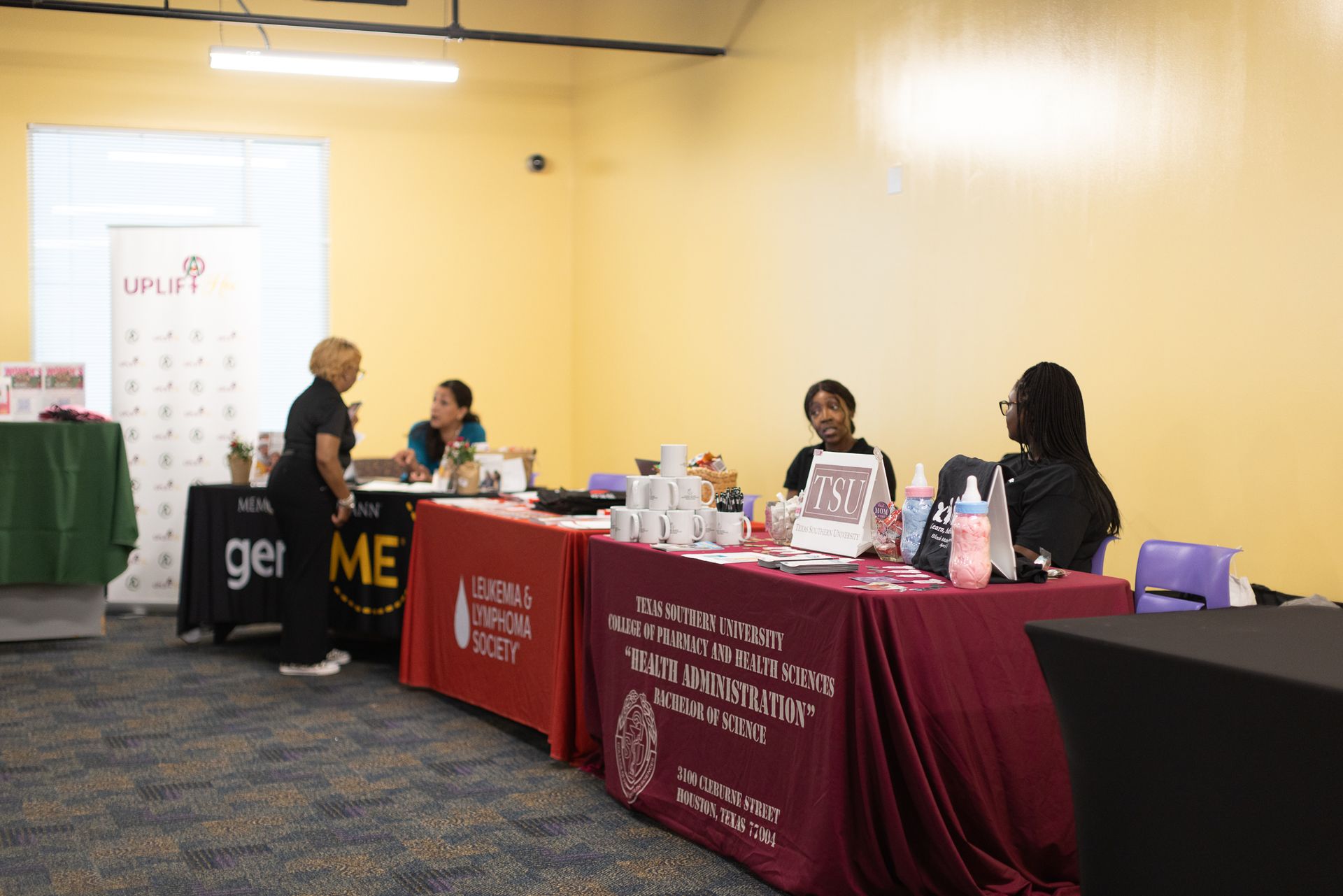 Tables with displays at an event; people behind them. Displays have products, information, and logo banners.