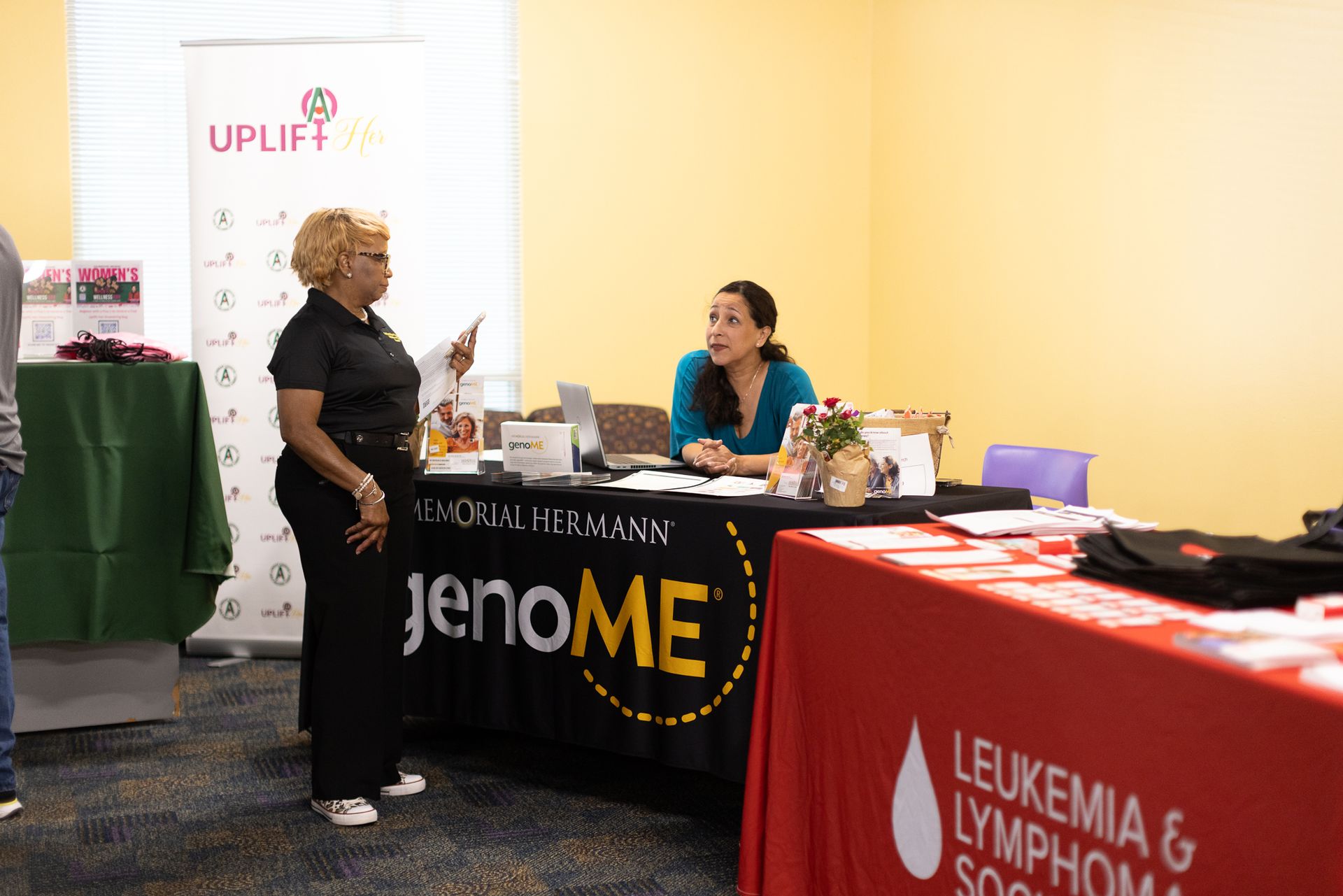Woman speaks to person at a table with banners 