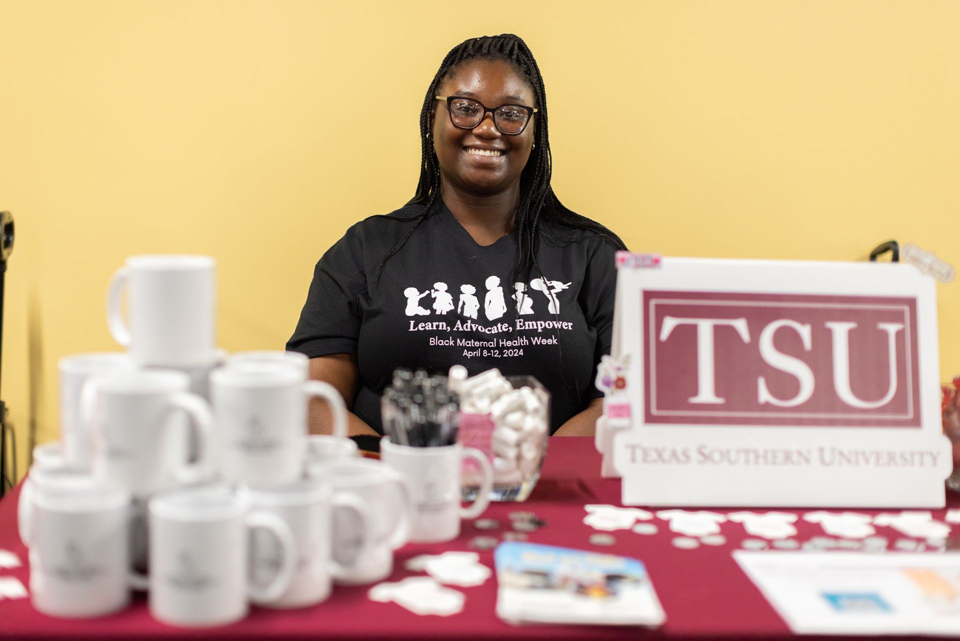 Woman at Texas Southern University table smiling, surrounded by TSU mugs and signs.