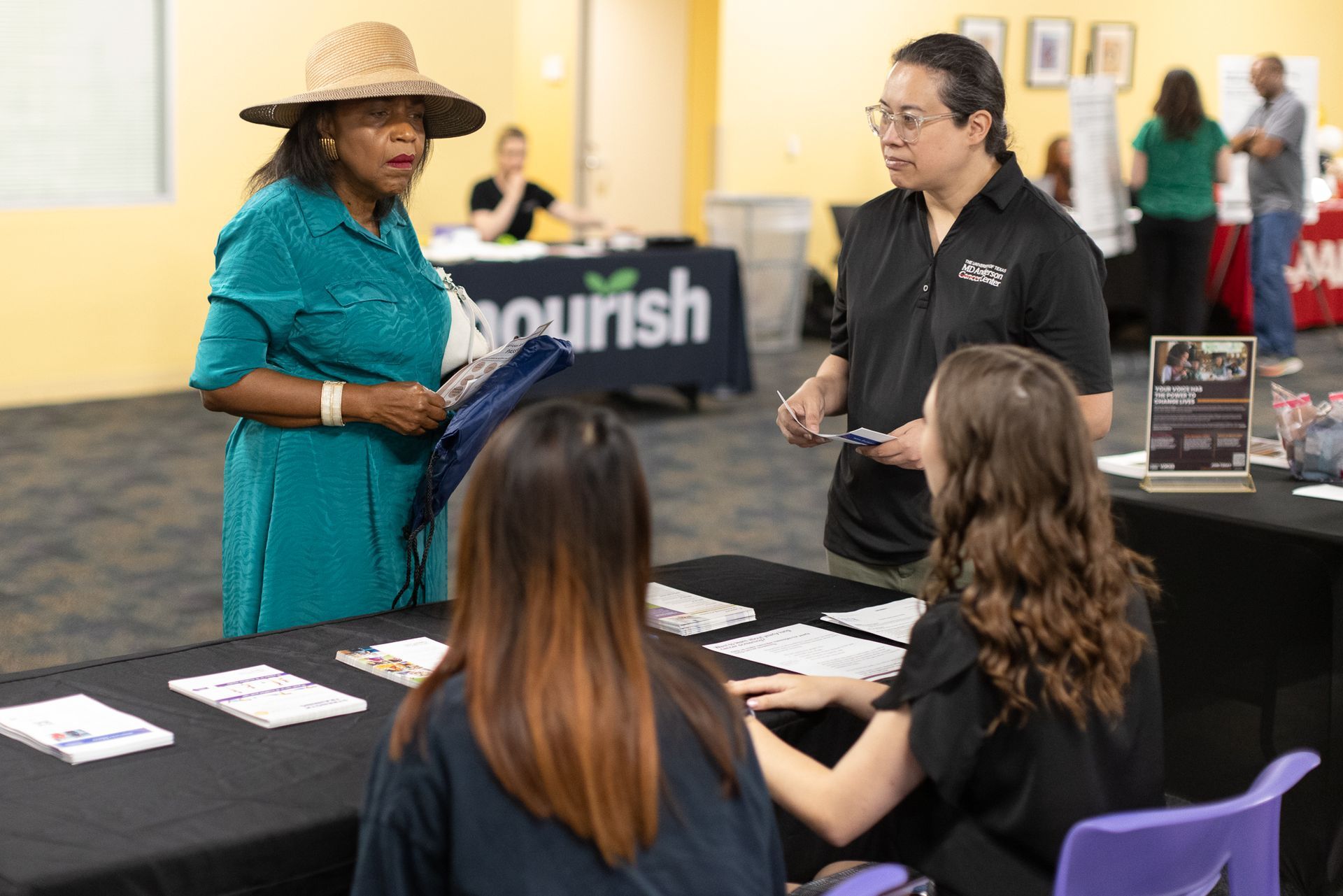 People at an informational booth, one wearing a hat. The booth has the word 