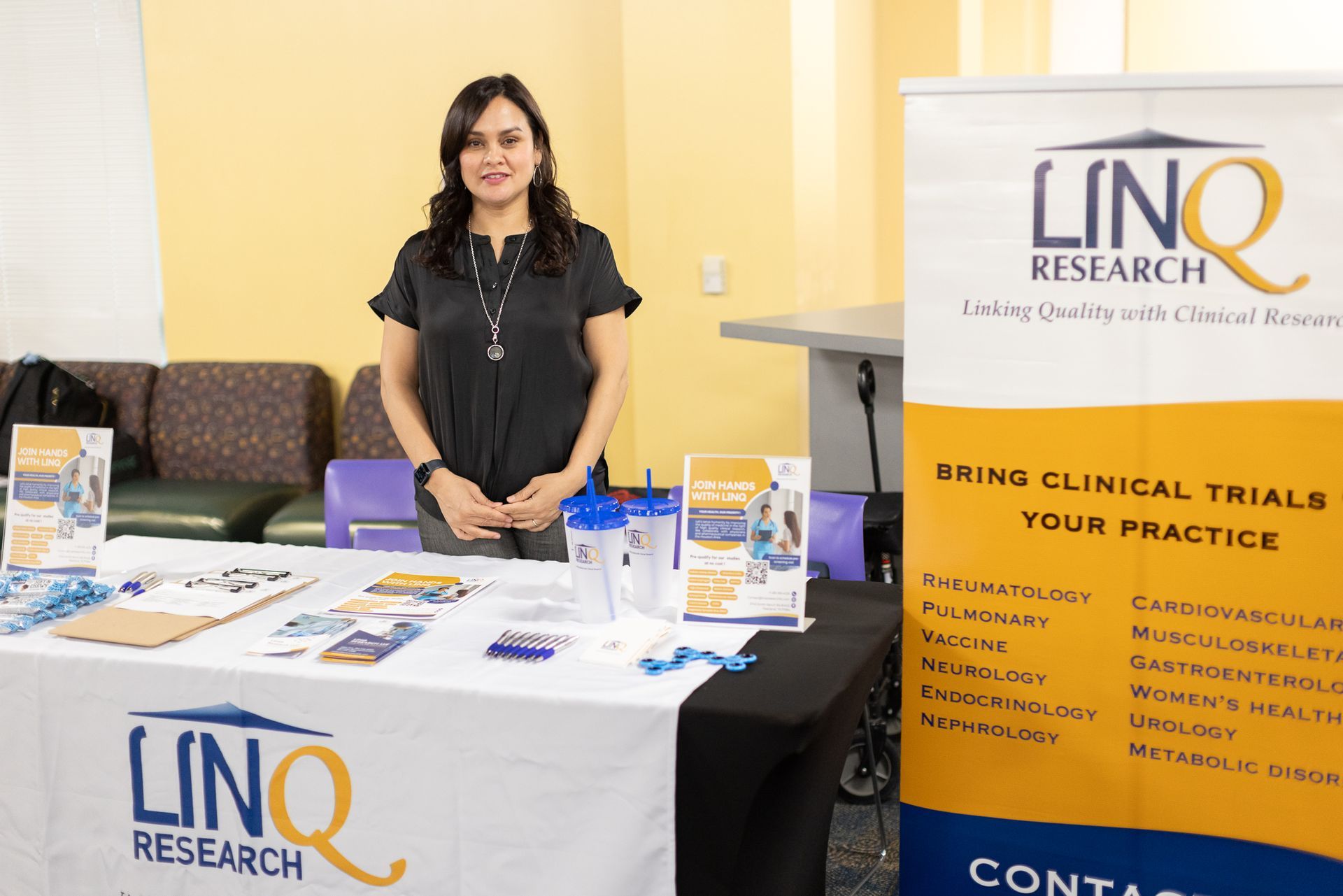 Woman at a booth for LINQ Research. The booth features materials and a banner promoting clinical trials.