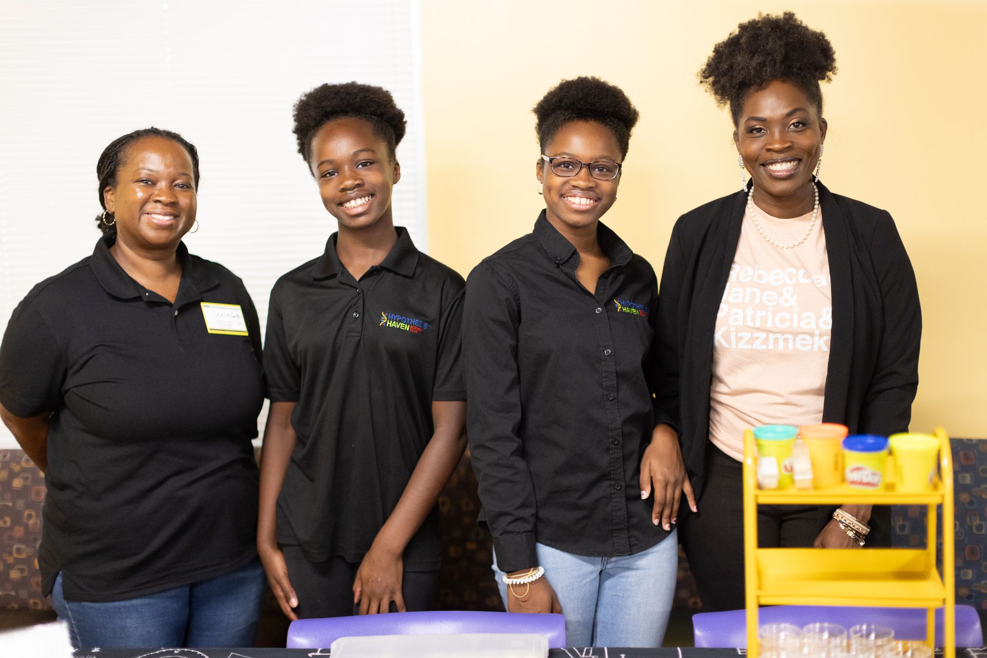 Four people standing behind a table with crafting supplies. They are smiling.
