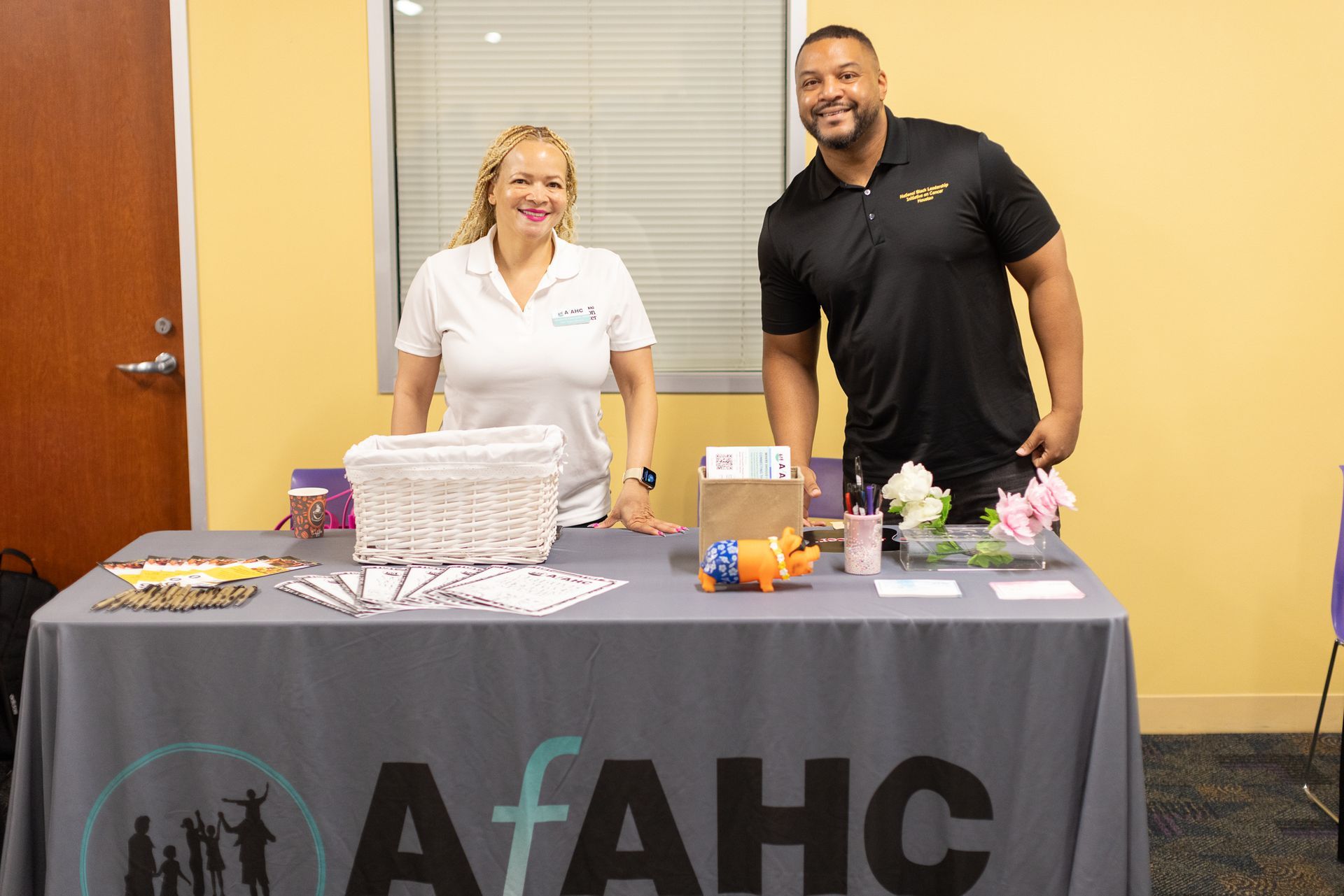 Two people at a table for AfAHC; the woman on the left smiles, the man on the right smiles.