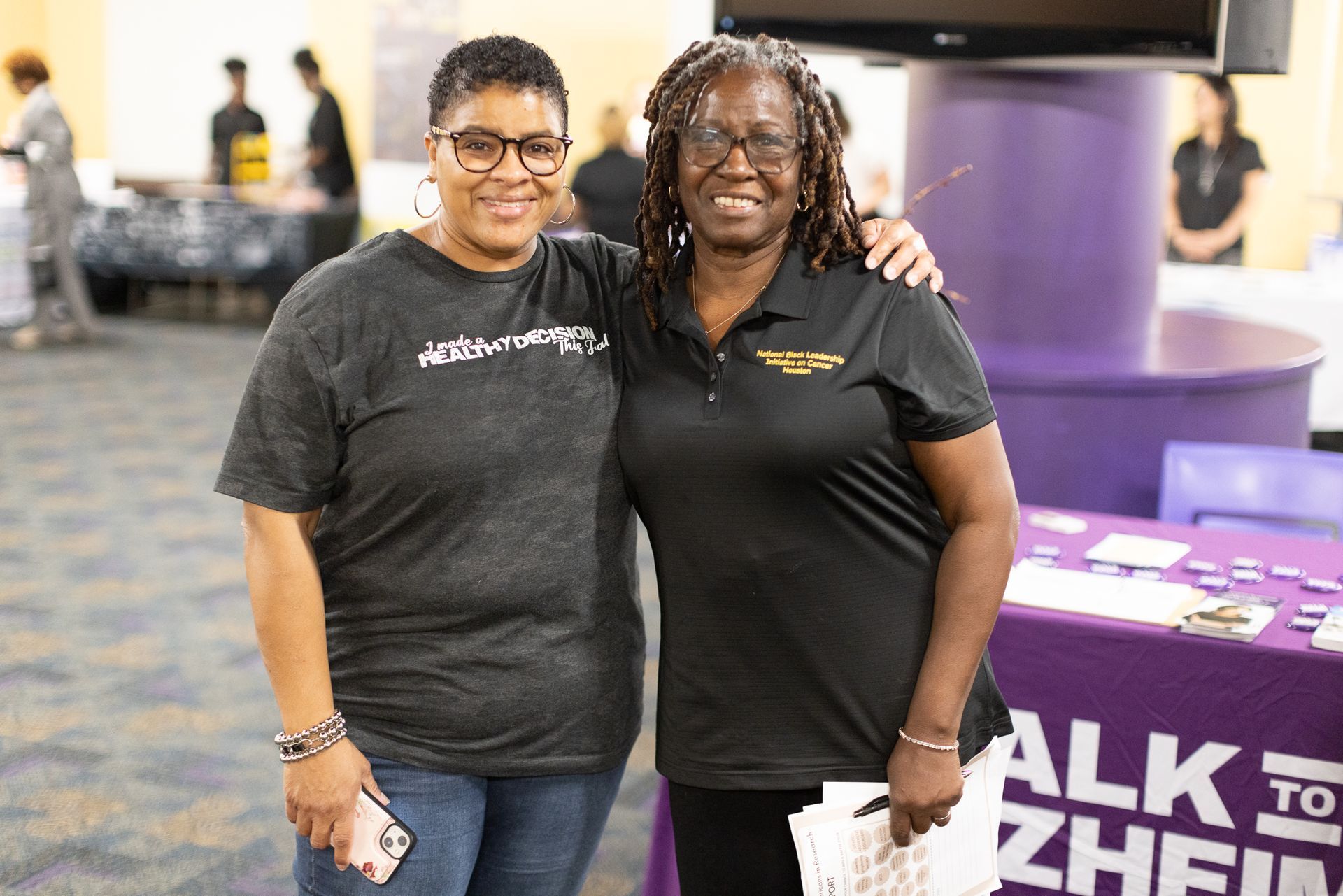 Two women smiling at camera, arm around each other, near a table with 