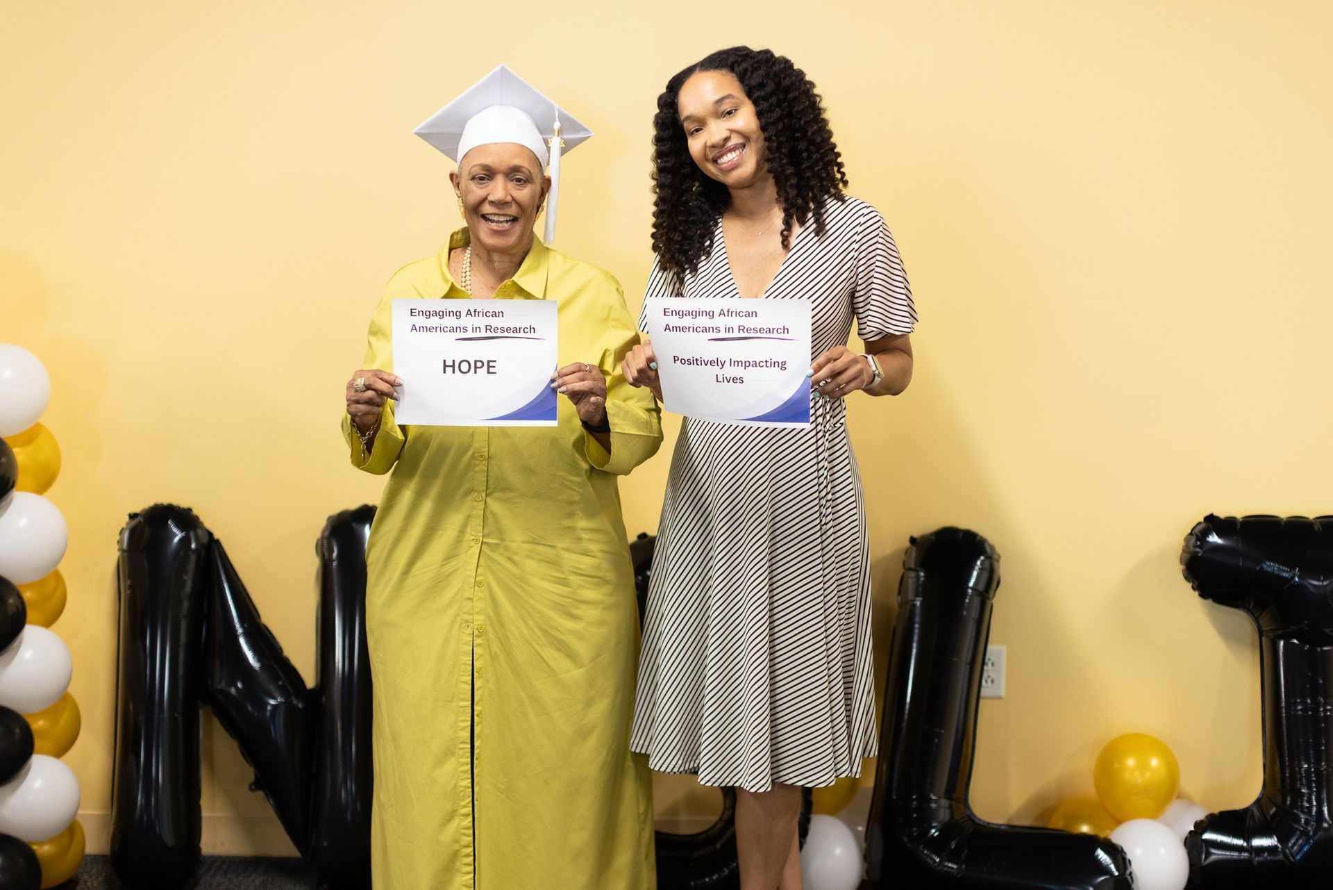 Two people holding certificates, celebrating in front of a graduation backdrop.
