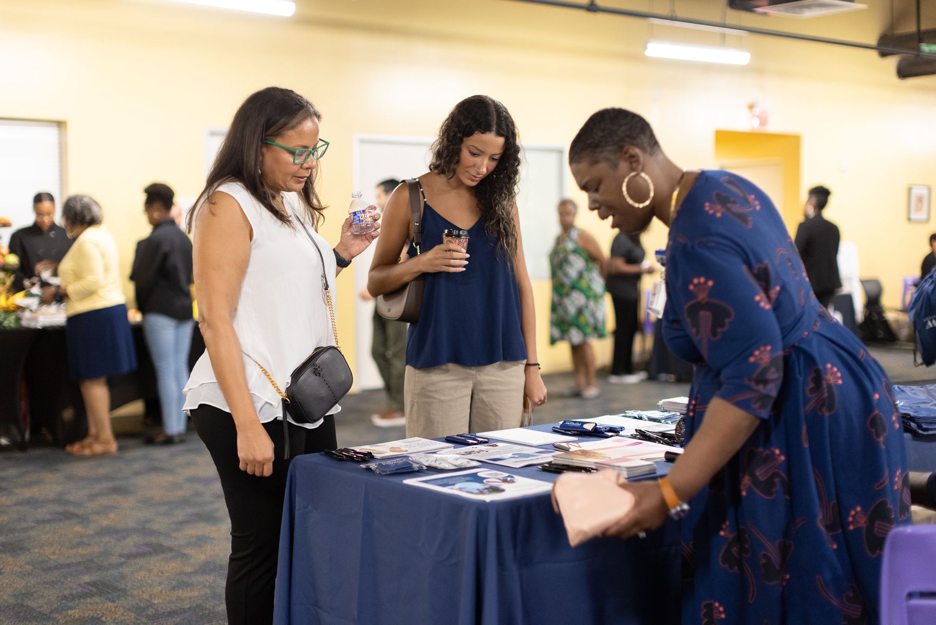 Three women at a table with brochures and a gift bag. Event setting.
