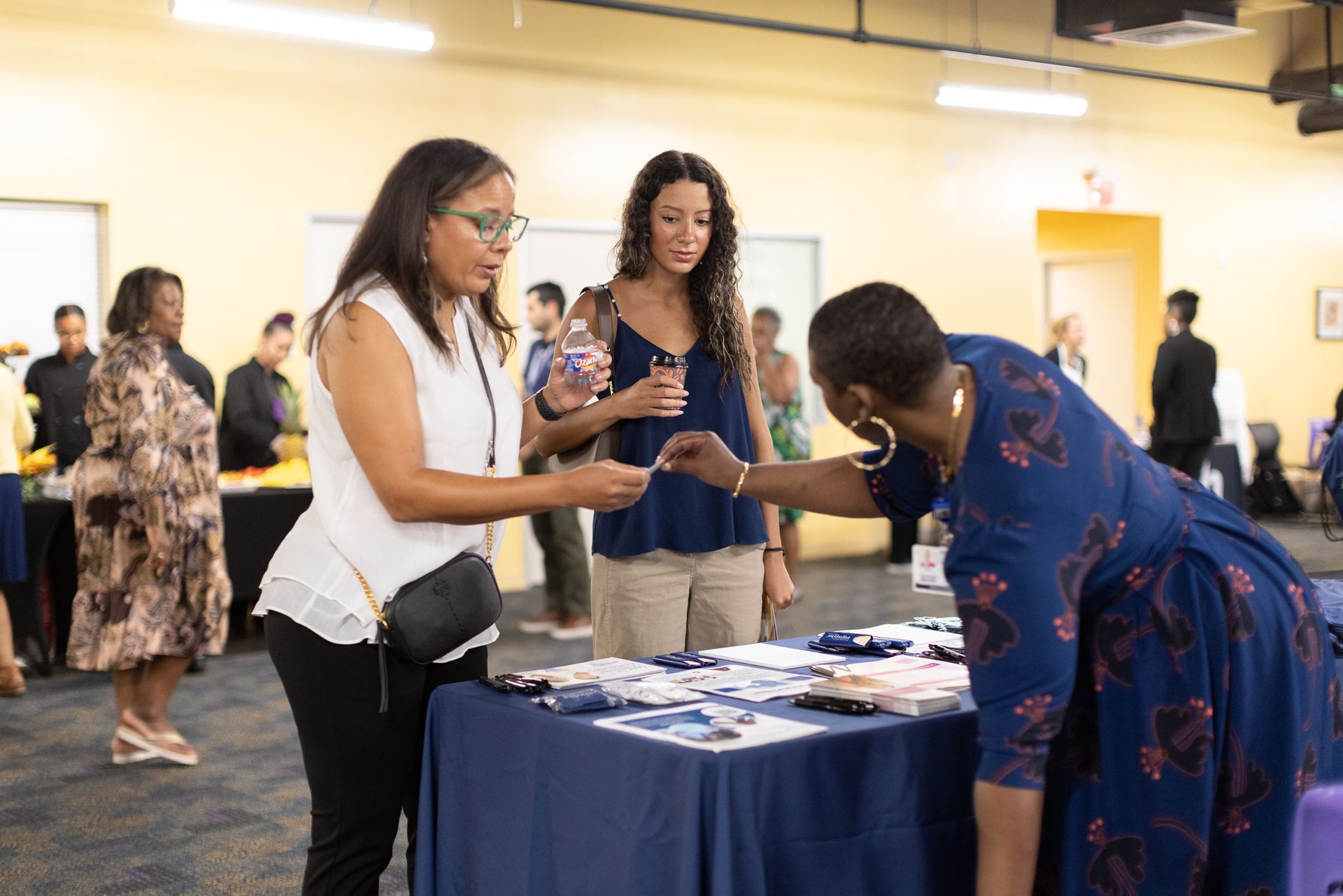 People at a table, one handing a card. Others look on in a room with a blue and yellow wall.