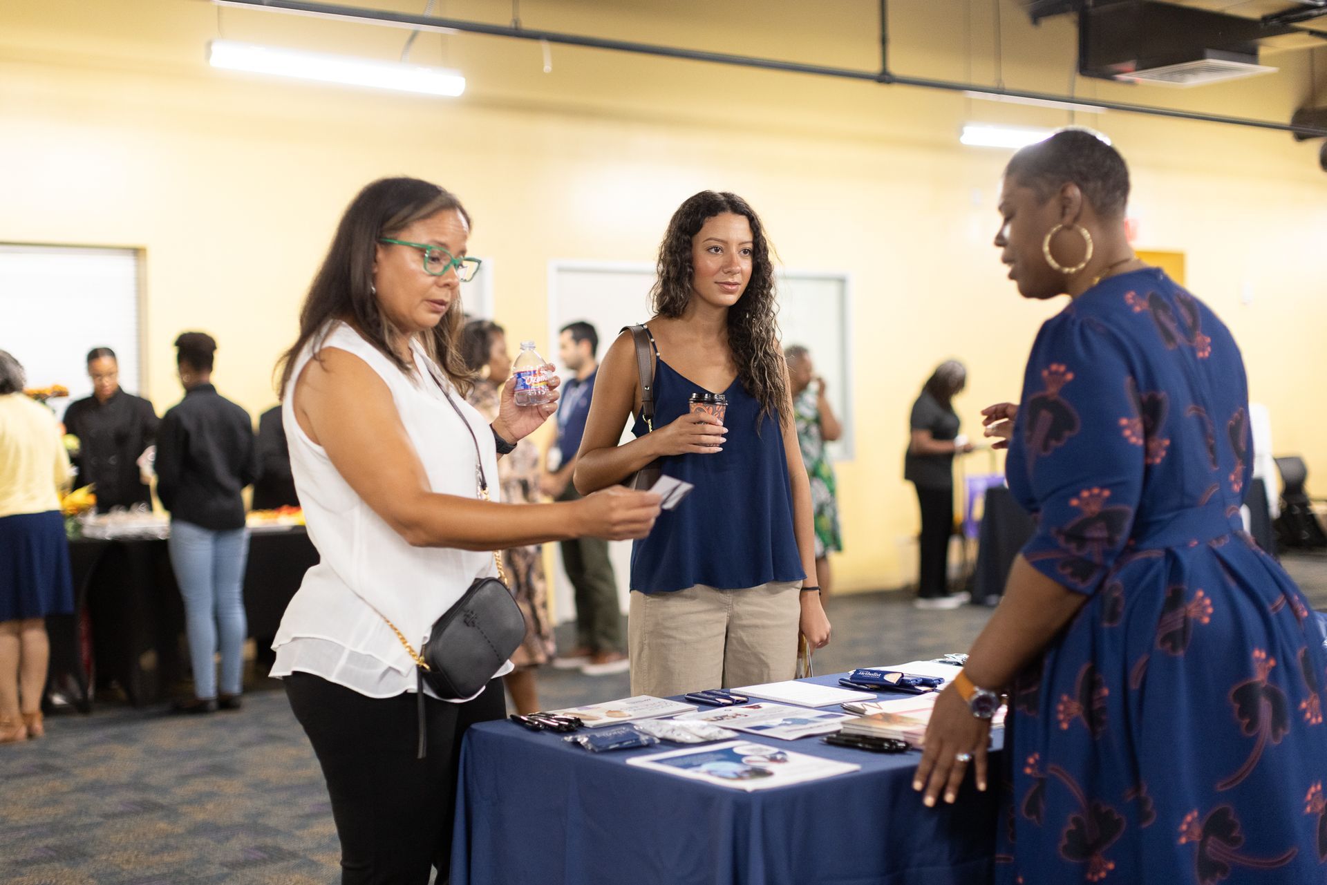 Three women at a table. One hands out a card. Event setting.