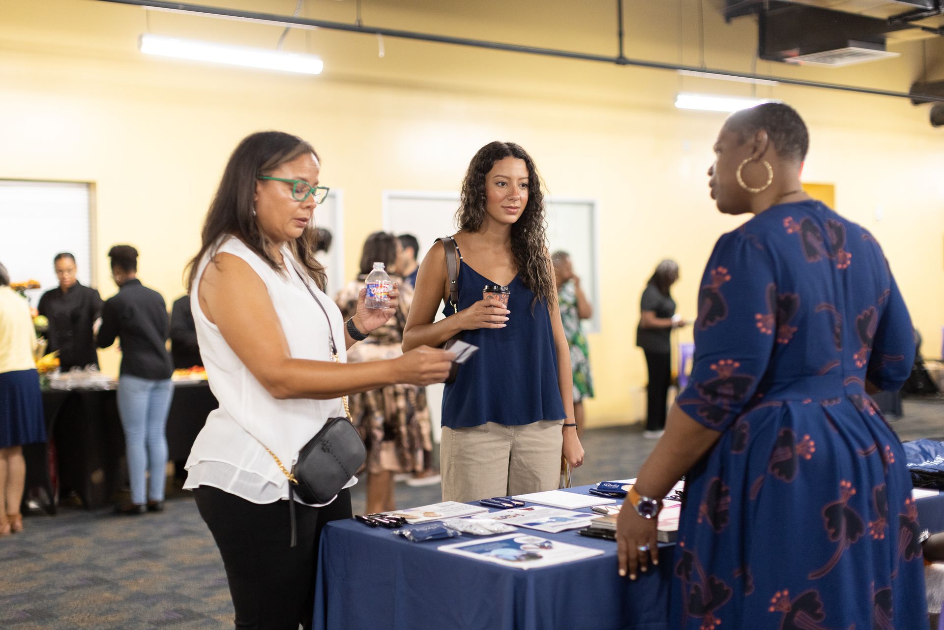 Three women conversing at an event, one is handing a paper.