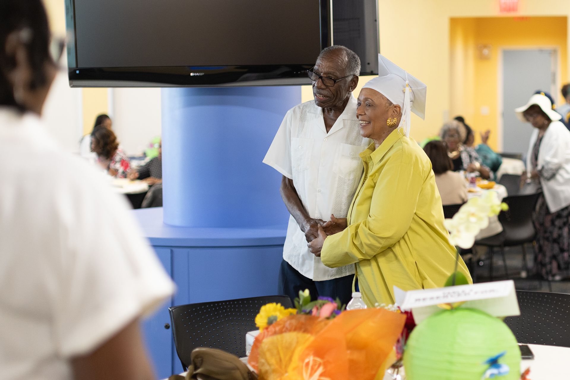 Elderly couple smiling, standing near decorated table in a community center.