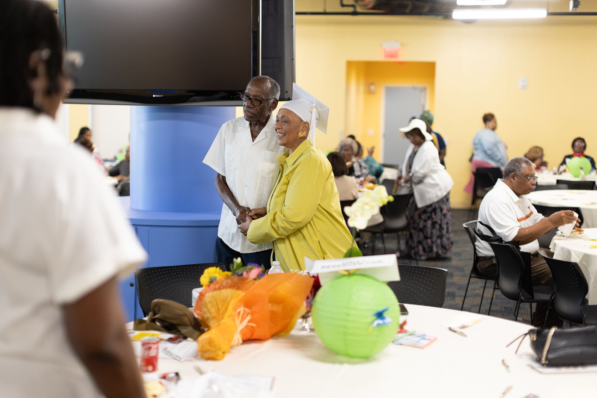 People at tables in a community room with crafts, one couple smiling in the foreground.