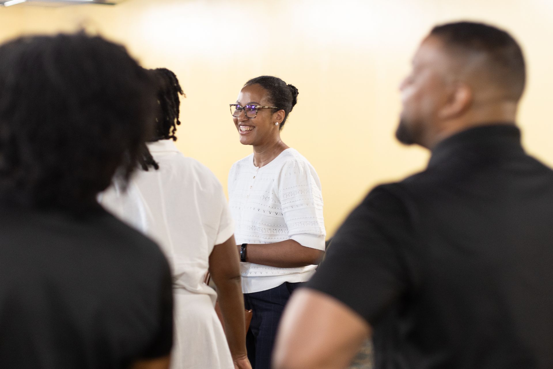 Group of people in a room, one smiling, wearing glasses.