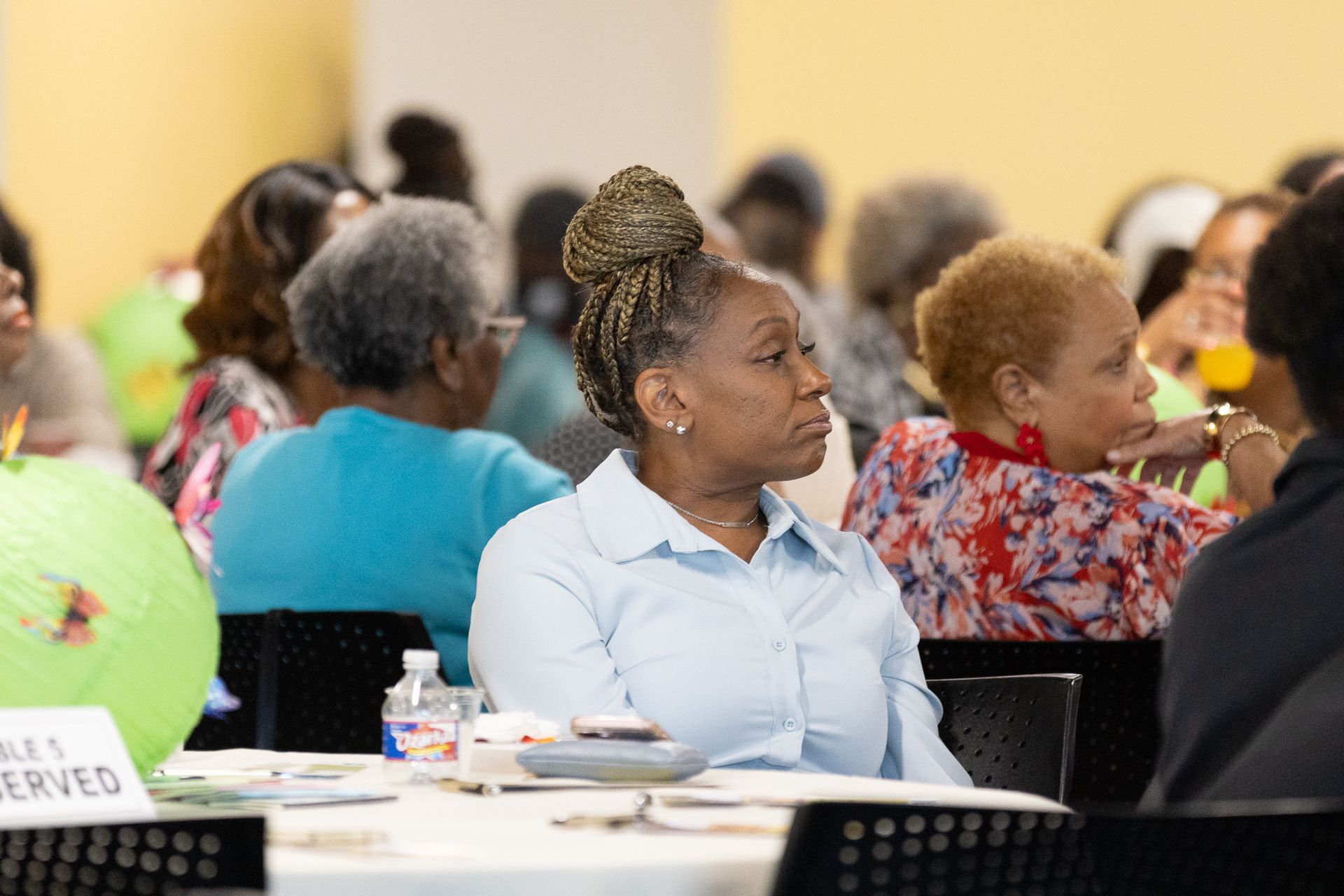 Woman with braided updo attends event, seated at table, looking to the side.