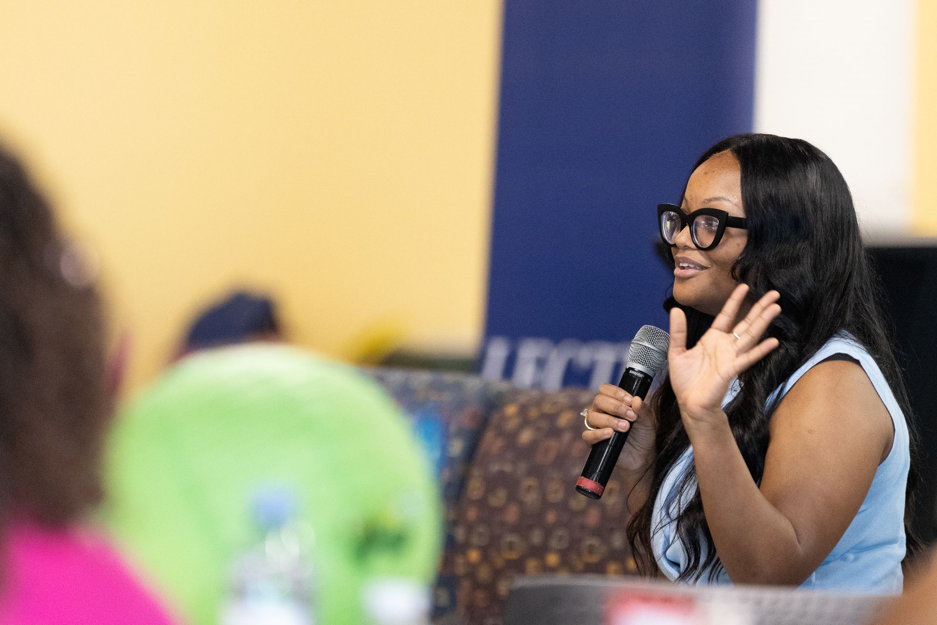 Woman speaking into a microphone, gesturing with her hand during a lecture.